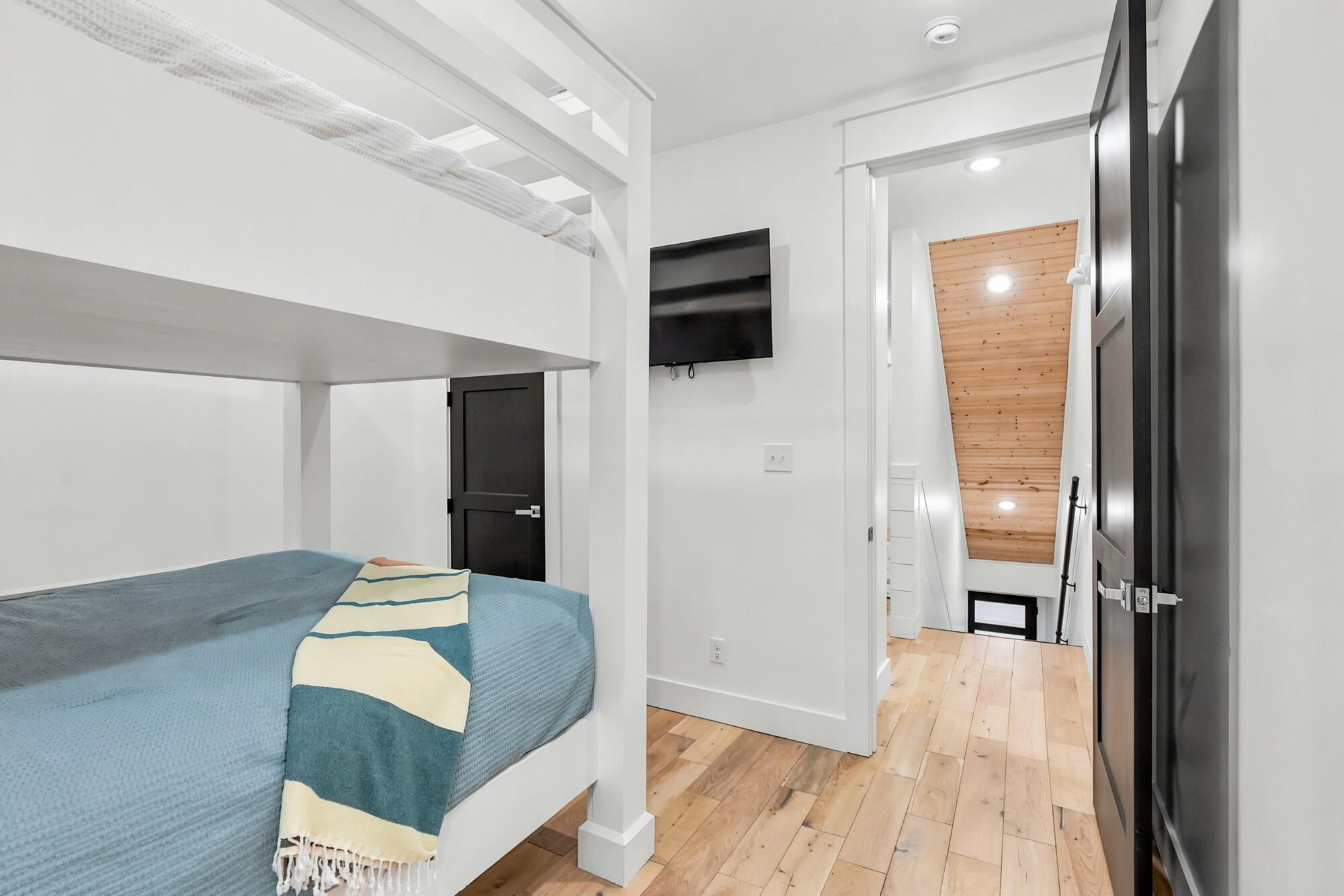 Bedroom with a white built-in bunk bed, blue bedding, and an adjoining hall with a wood ceiling.