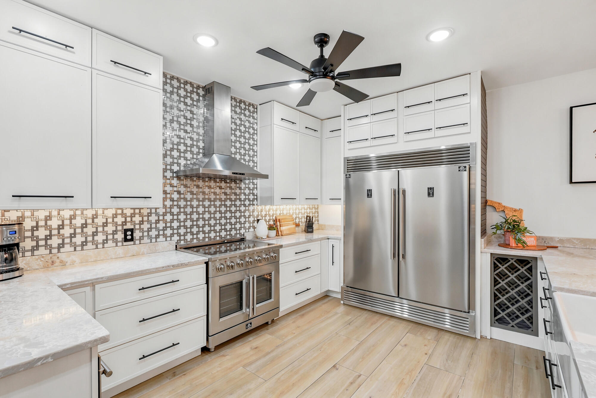 Modern white kitchen with geometric backsplash, stainless steel appliances, and a large built-in refrigerator.