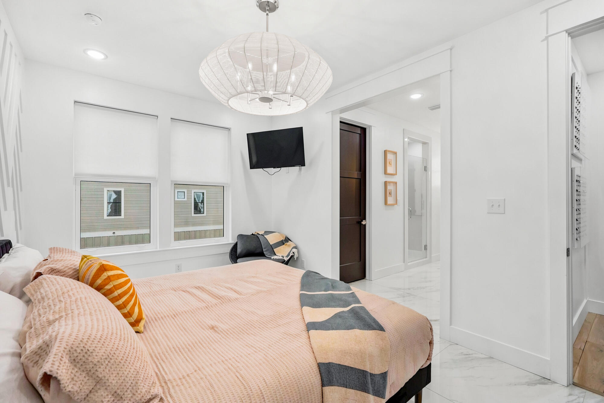 Furnished bedroom with a blush bed, striped throw, wall-mounted TV, and woven pendant light.