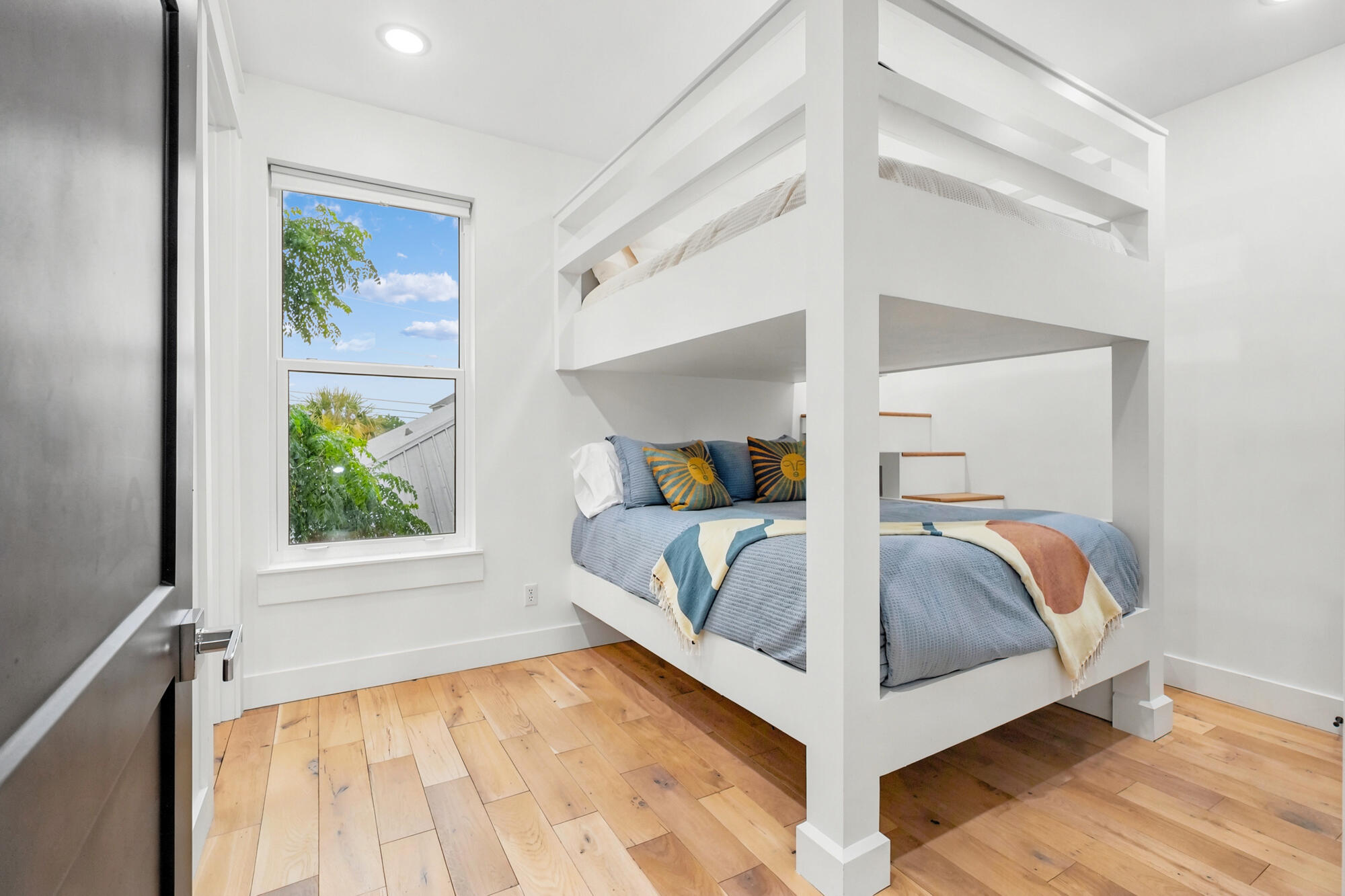 Bedroom with a white built-in bunk bed, blue bedding, and light wood flooring.