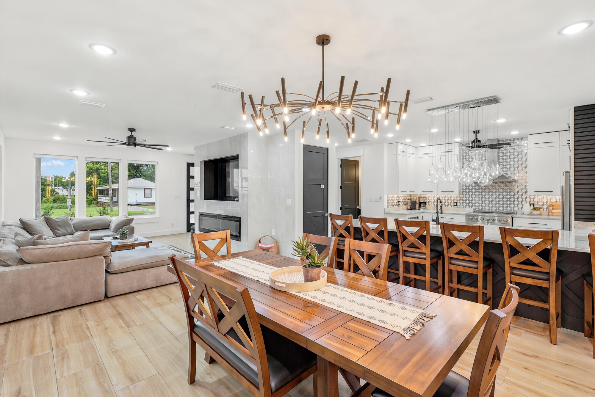 Open-plan dining room, living room, and kitchen with a wood table, white cabinets, and sculptural chandelier.