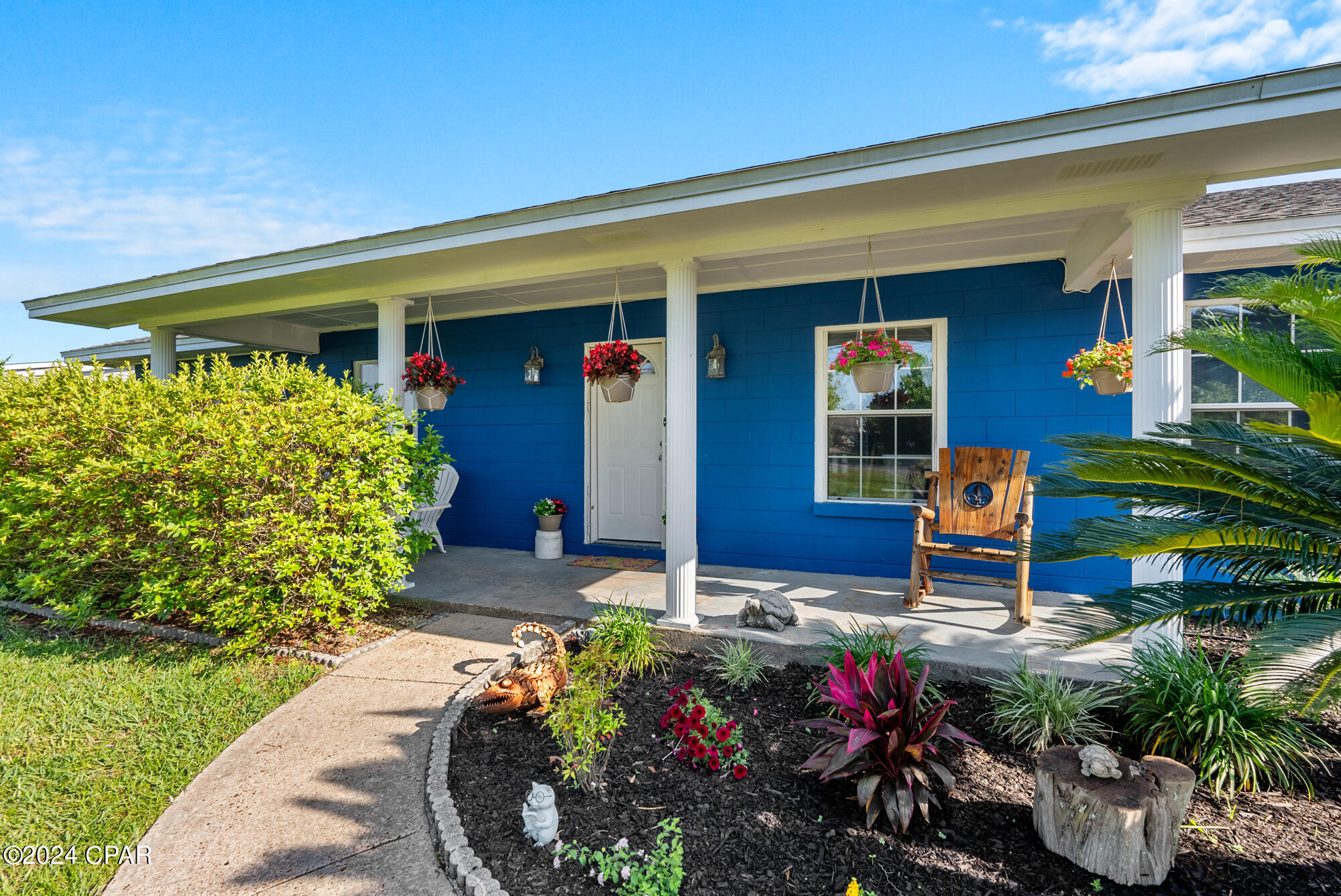 Blue house with a white-columned porch, hanging flowers, and a landscaped garden path.