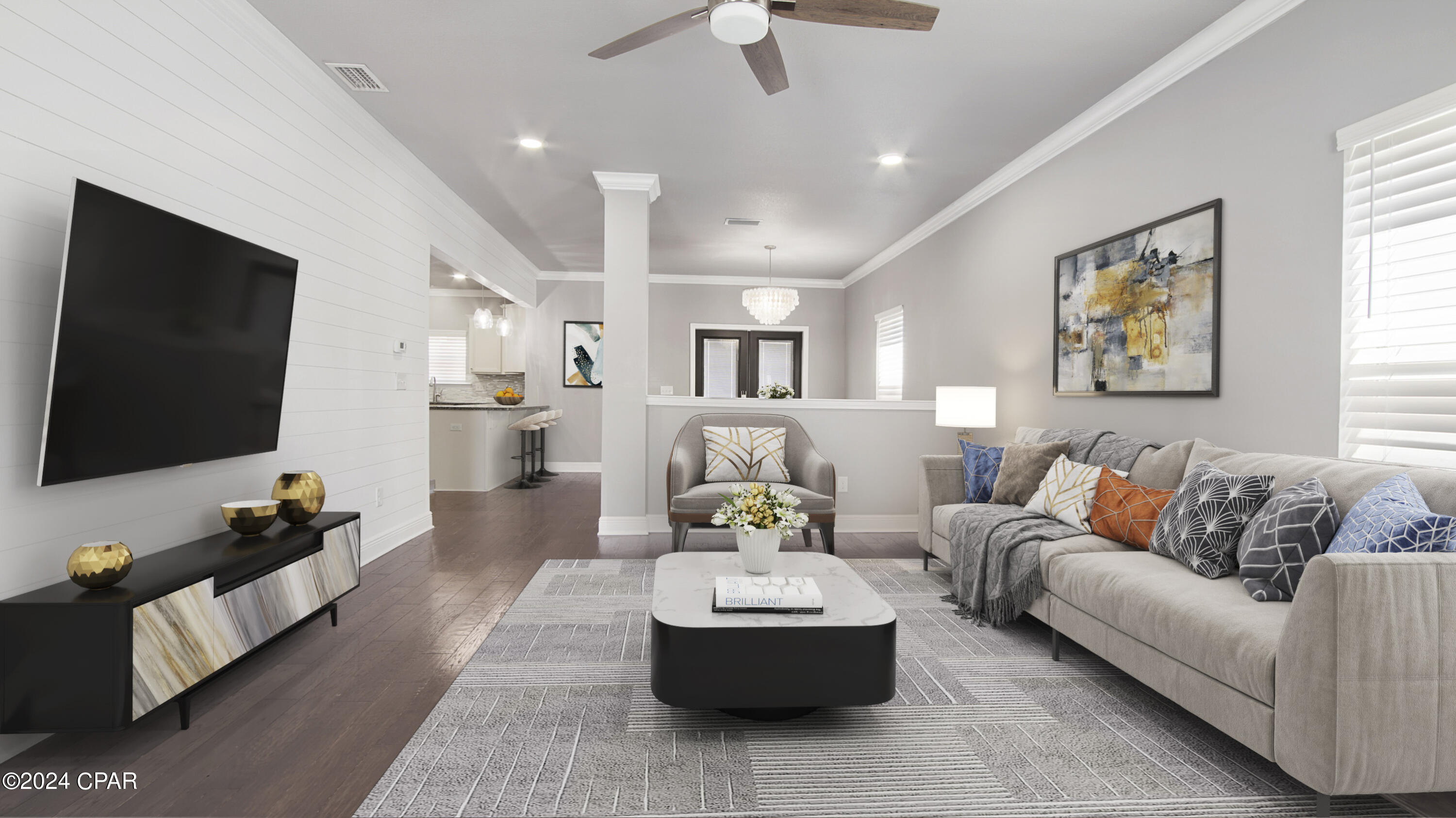 Staged living room with gray sofas, a large patterned rug, and an open view toward the kitchen.