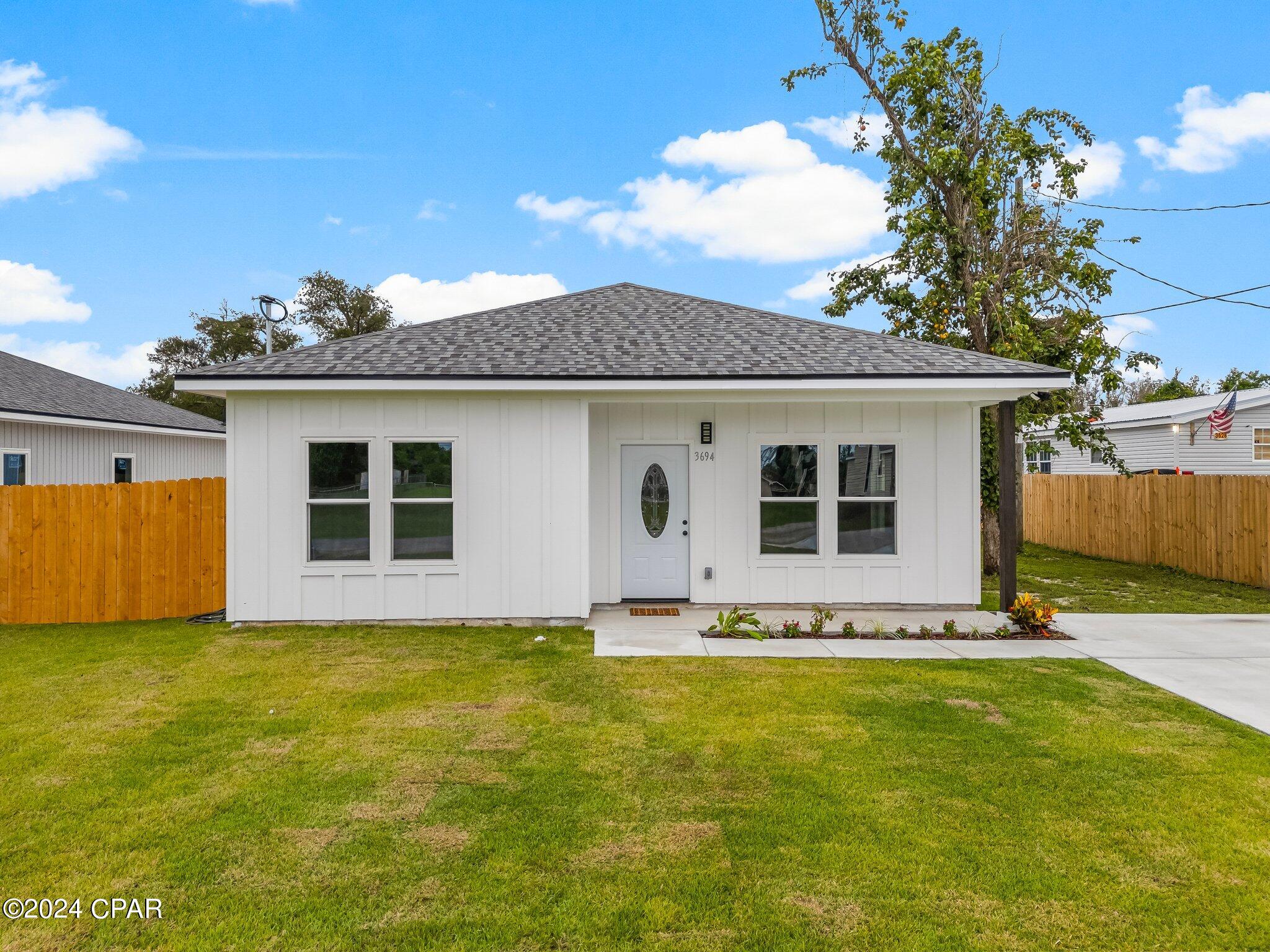 White single-story house with an oval-glass front door, gray roof, and fenced lawn.