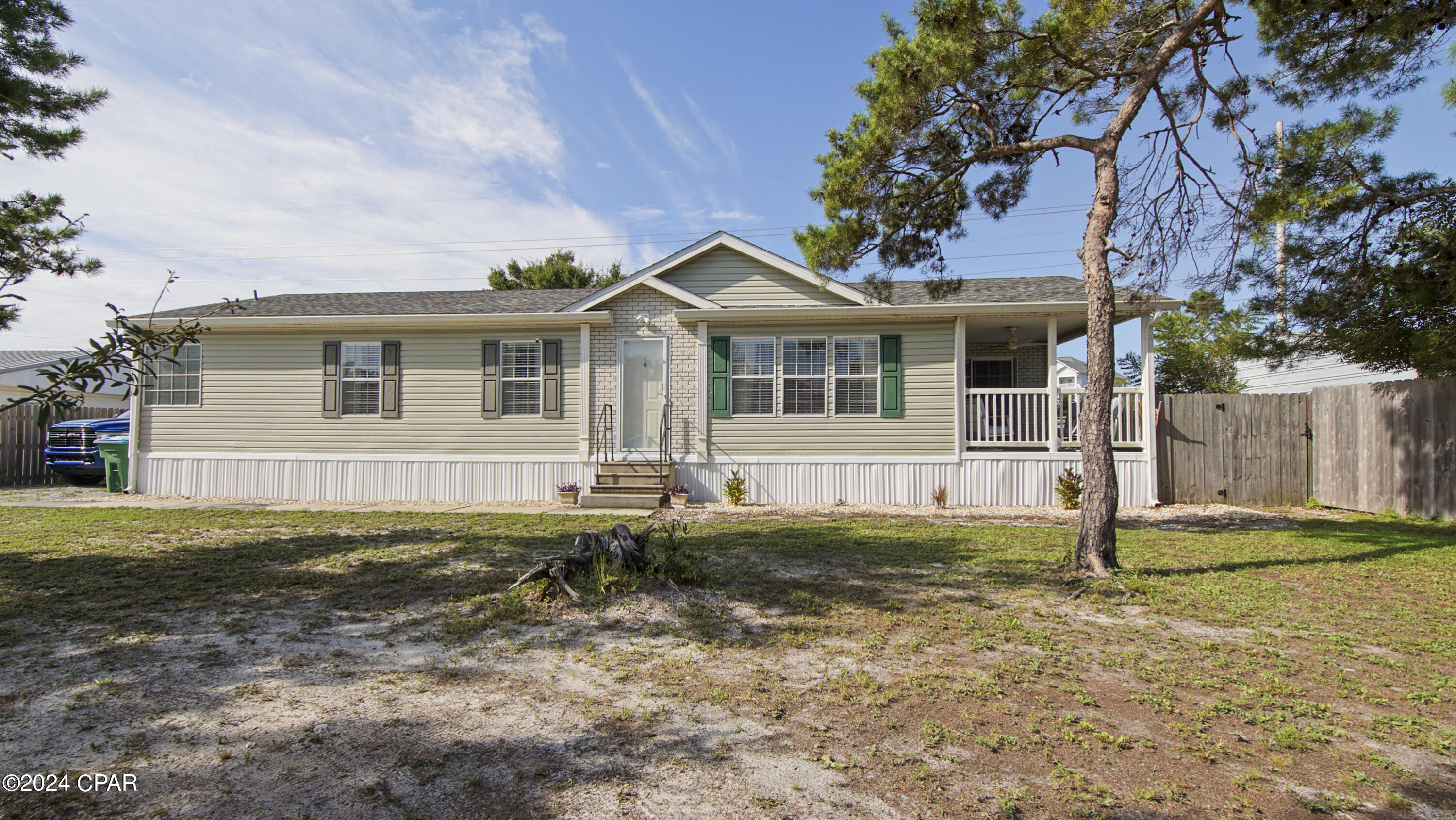 Beige single-story home with green shutters, a covered porch, and a large pine tree in the yard.