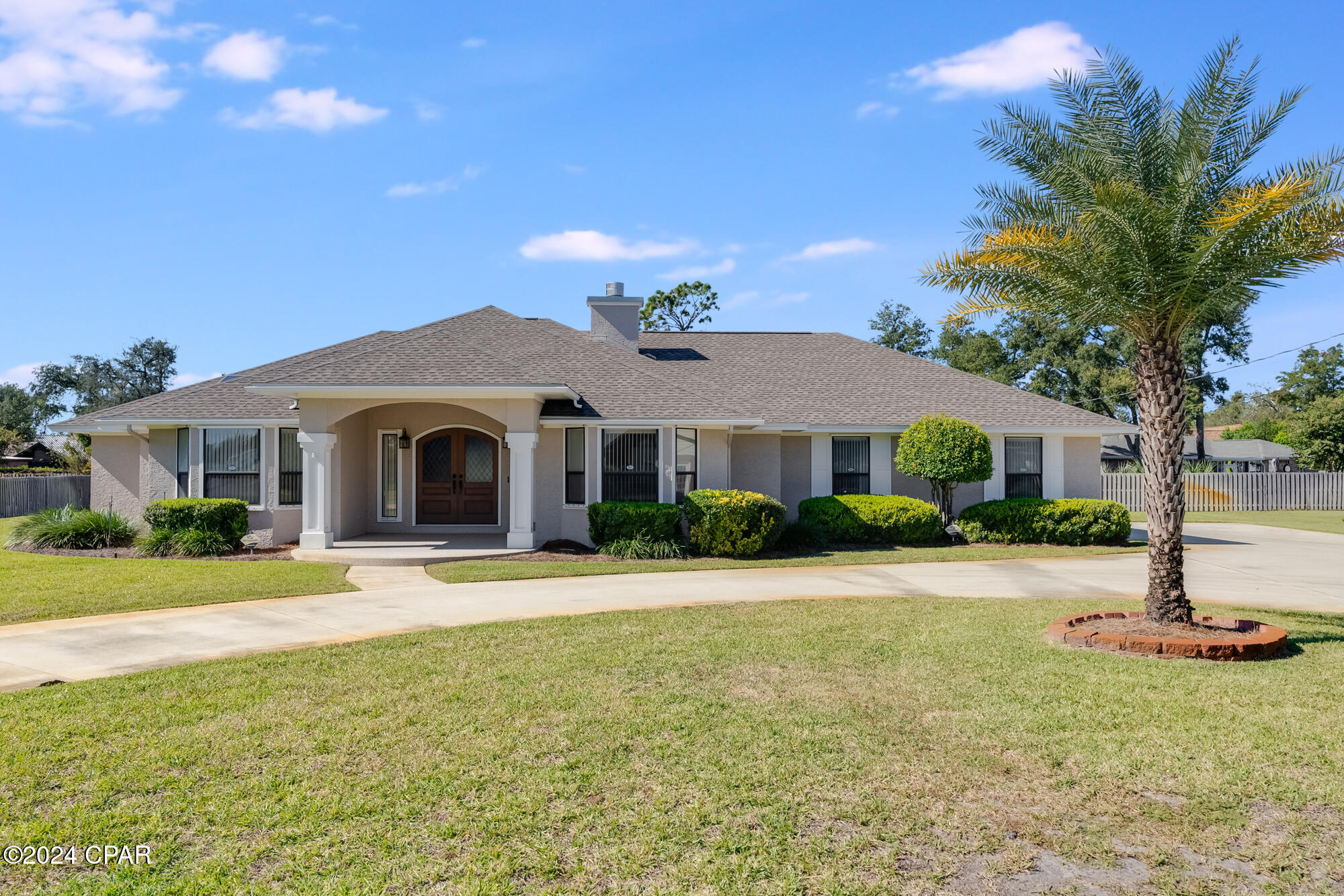 Single-story stucco home with a covered entry porch, front lawn, and tall palm tree.