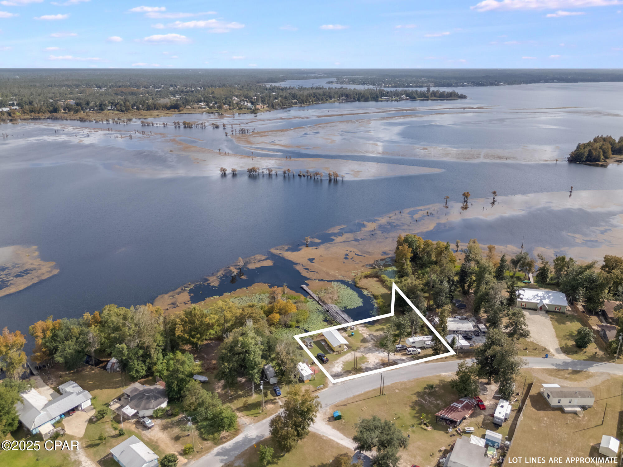 Aerial view of a waterfront lot outlined in white, with a dock and wooded shoreline.