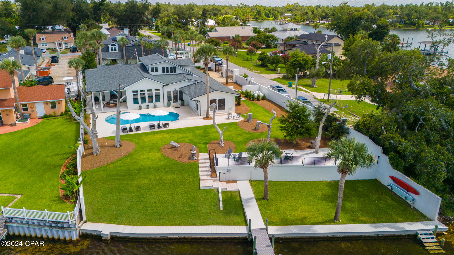 Waterfront home with a pool, broad green lawn, raised patio, and dock.