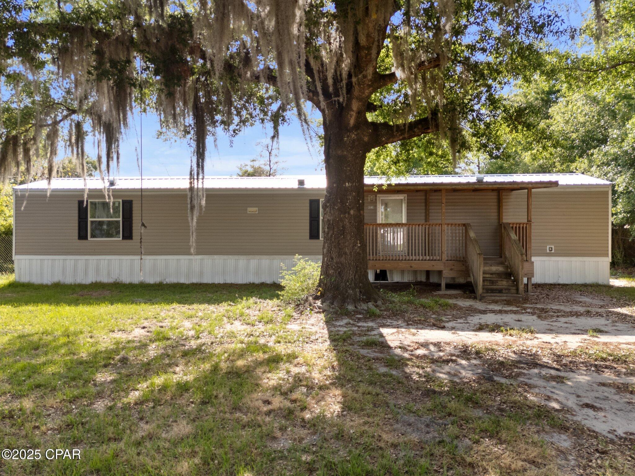Manufactured home with a raised wooden porch beneath a large oak draped in Spanish moss.
