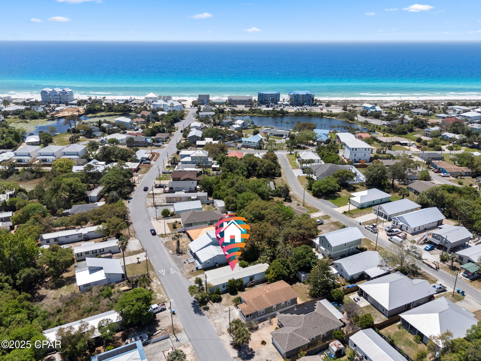 Aerial coastal neighborhood with a lagoon, oceanfront beach, and colorful house-shaped map marker.
