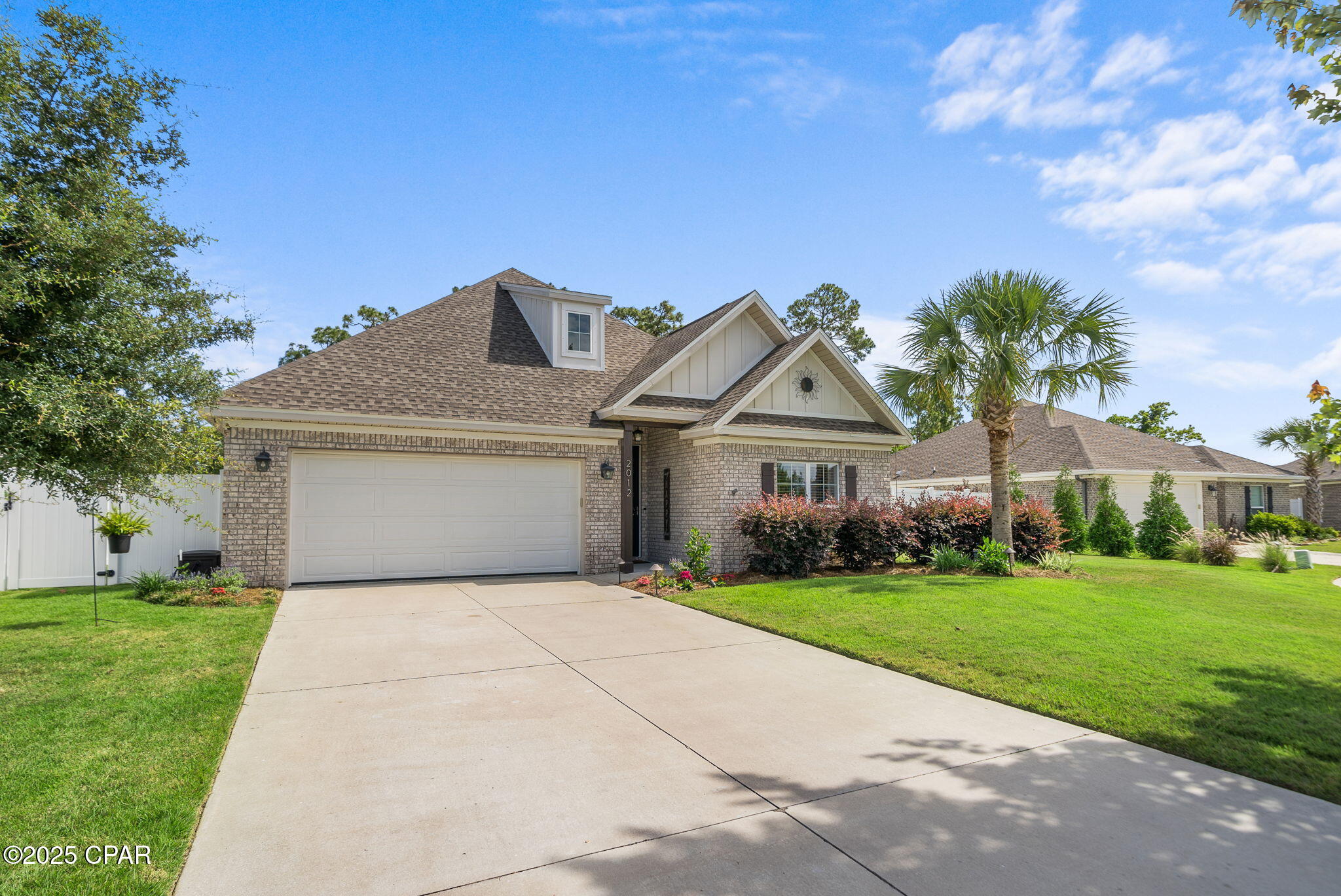 Brick house with a two-car garage, palm tree, landscaped lawn, and wide driveway.