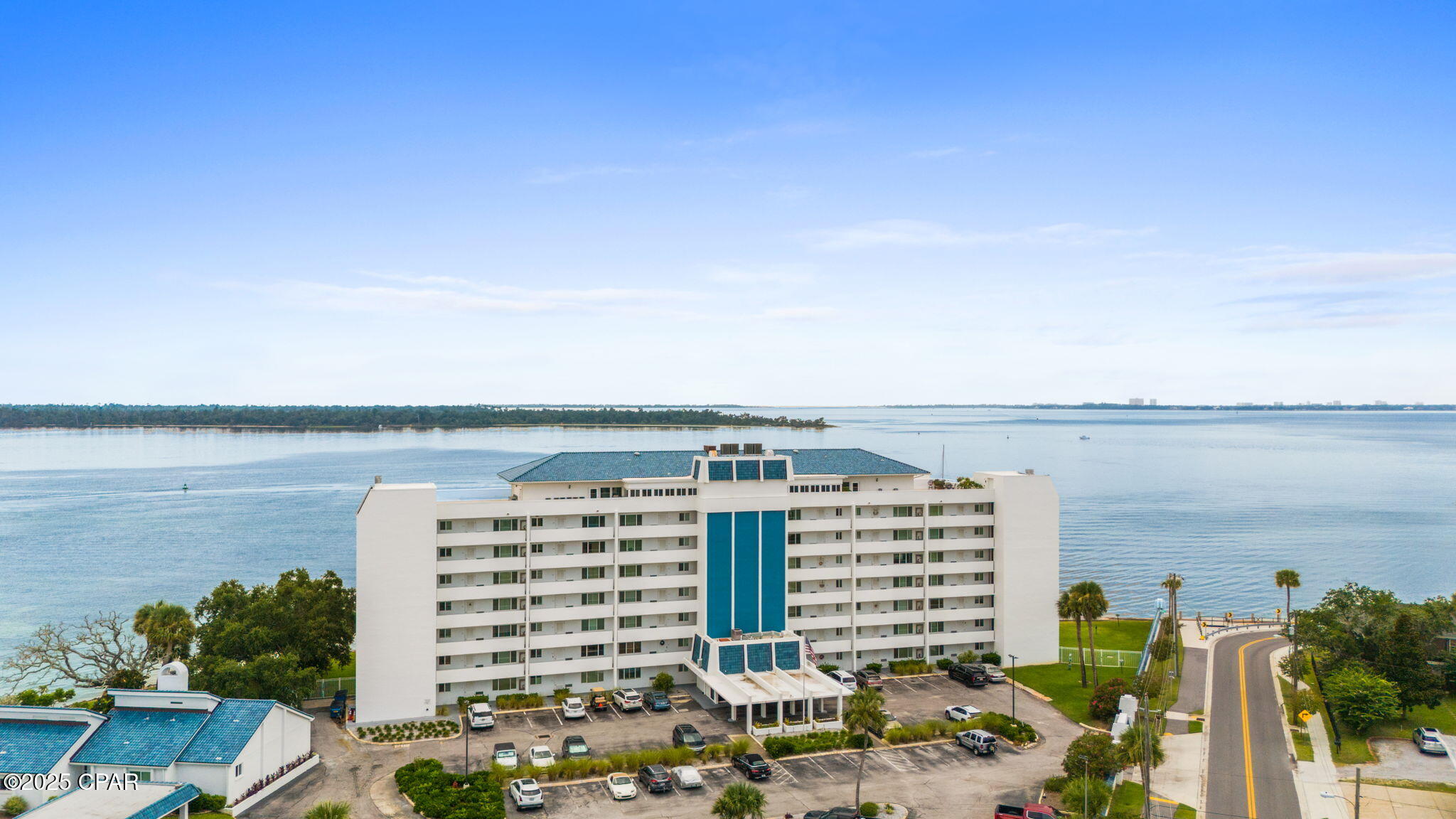 Waterfront condominium with blue roof accents and balconies beside a broad bay.