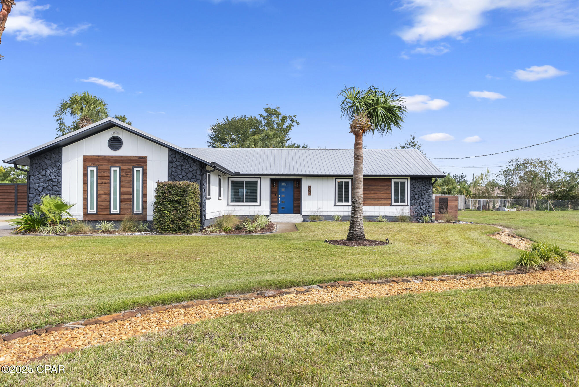 Single-story ranch home with dark stone accents, wood-look panels, and a blue front door.
