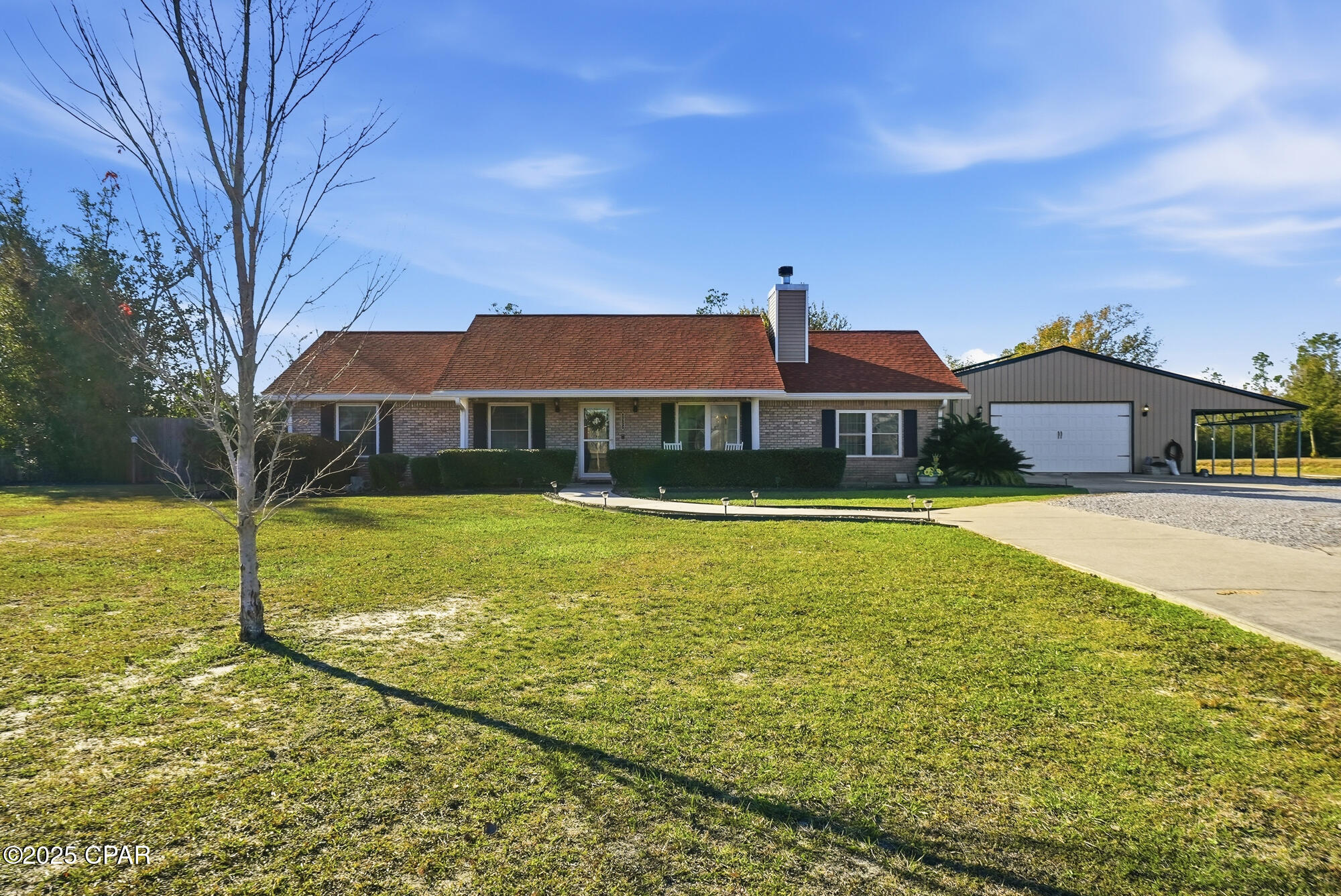 Single-story brick house with a broad lawn, curved walkway, and garage with an open-sided carport.