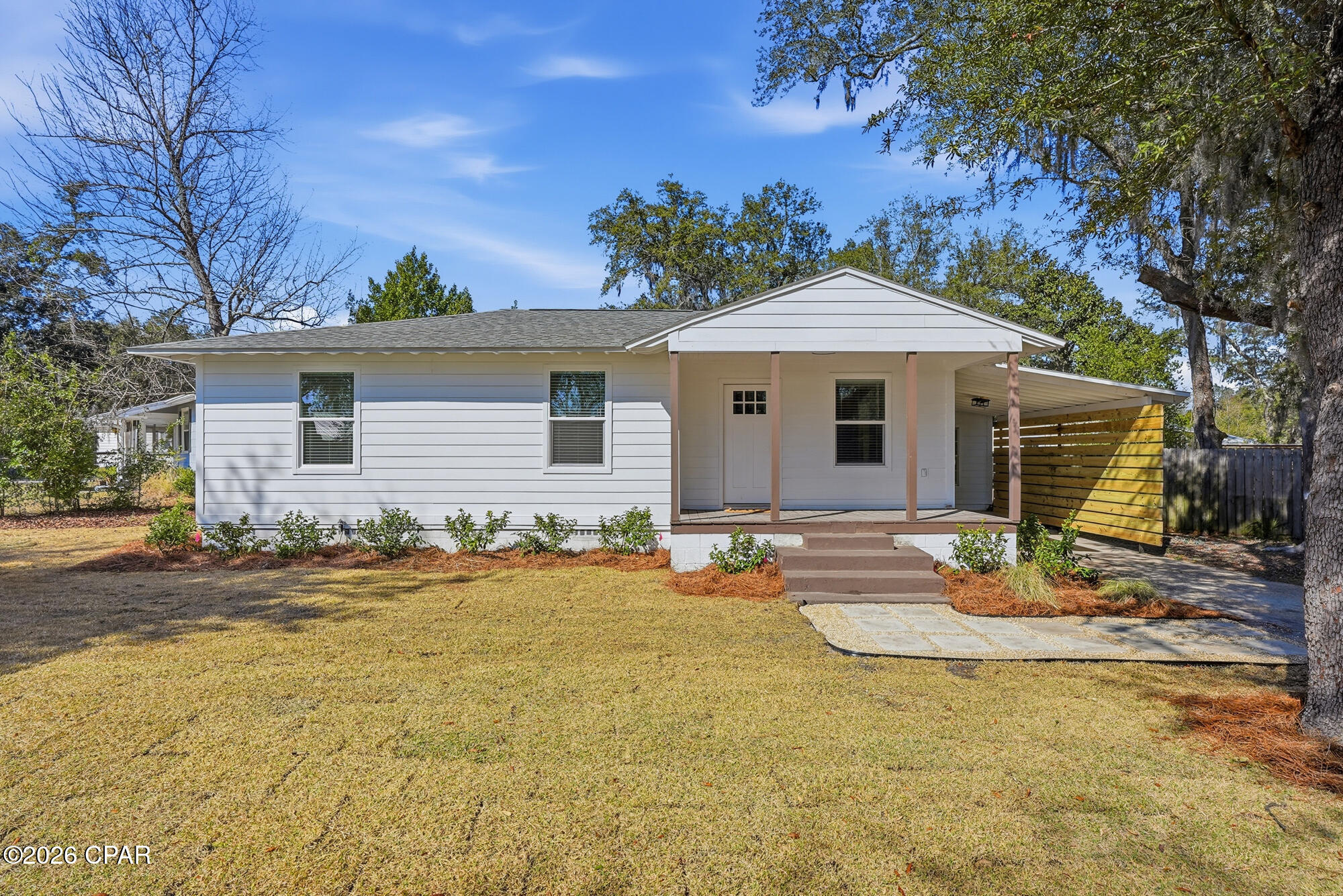 White single-story house with a covered front porch and wooden privacy screen beside the driveway.