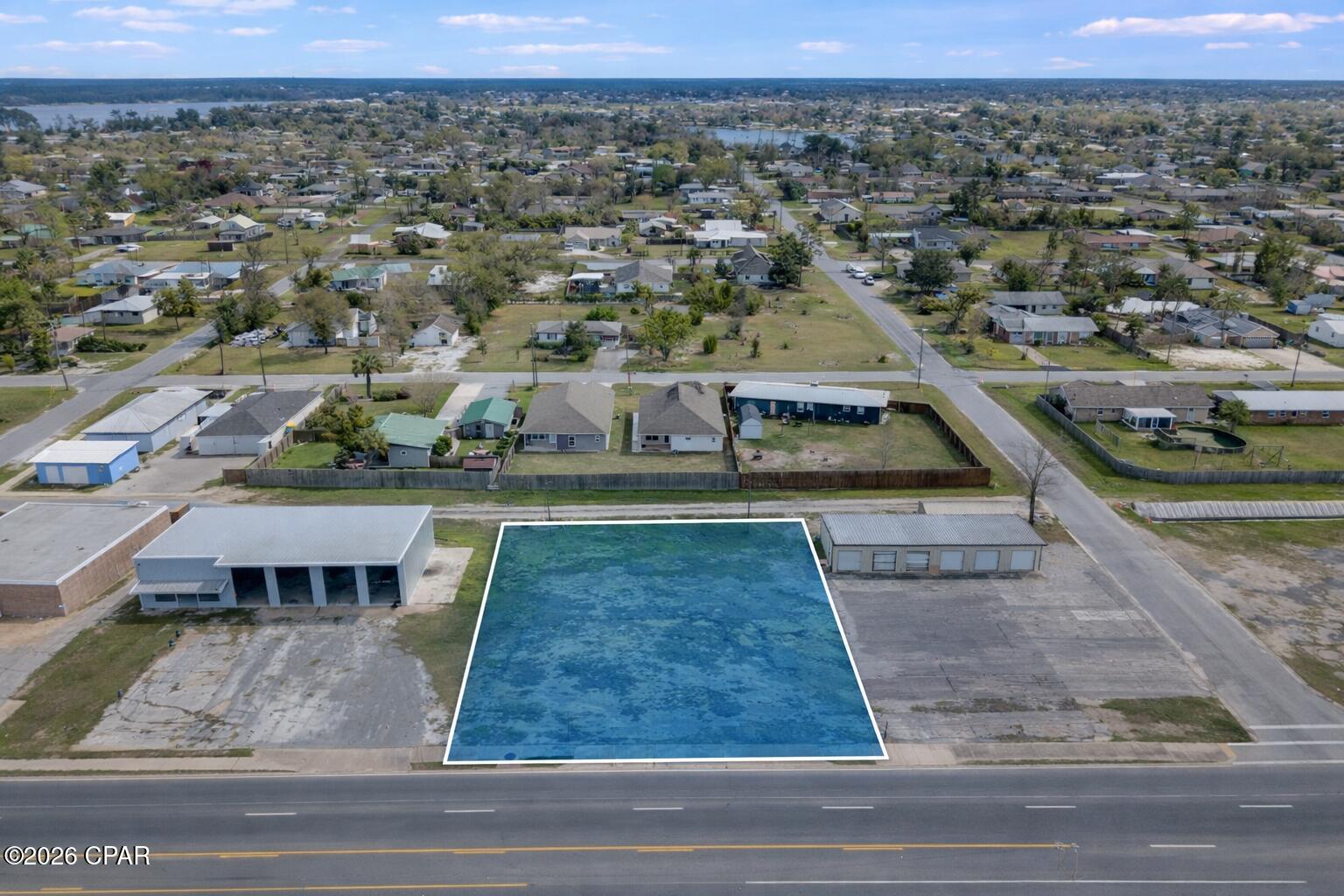 Aerial view of a blue-highlighted roadside lot, with homes and water in the distance.