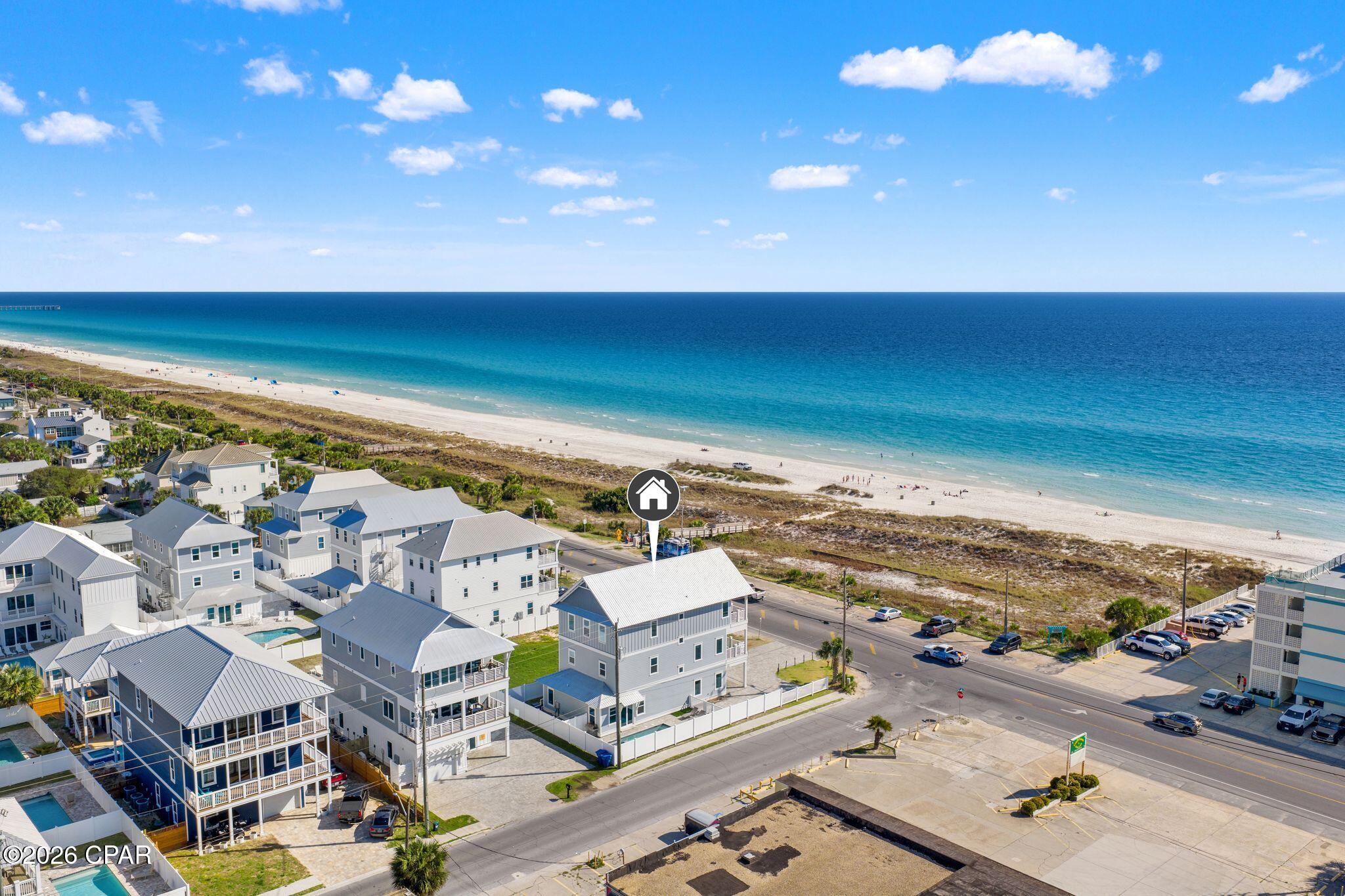Coastal home marked near a sandy beach, with turquoise water and neighboring houses.