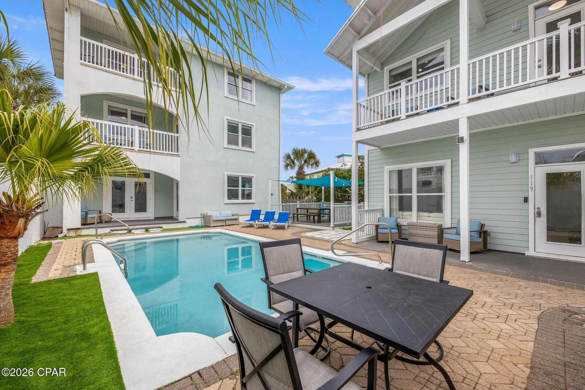 Pool courtyard between two coastal-style homes, with balconies, patio seating, and palm trees.