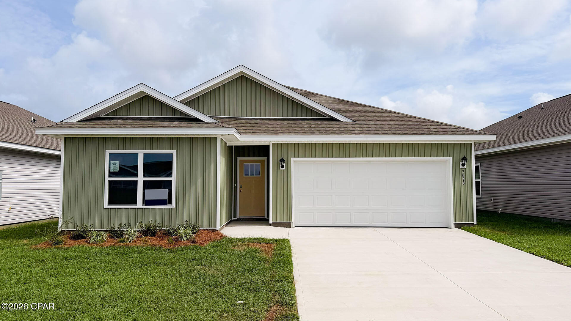 Green-sided single-story house with a white double garage and wide concrete driveway.