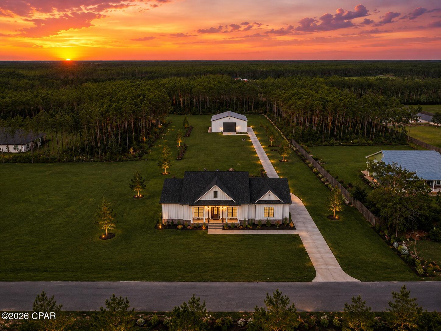 Aerial view of a white farmhouse and landscaped acreage beneath a vivid sunset.