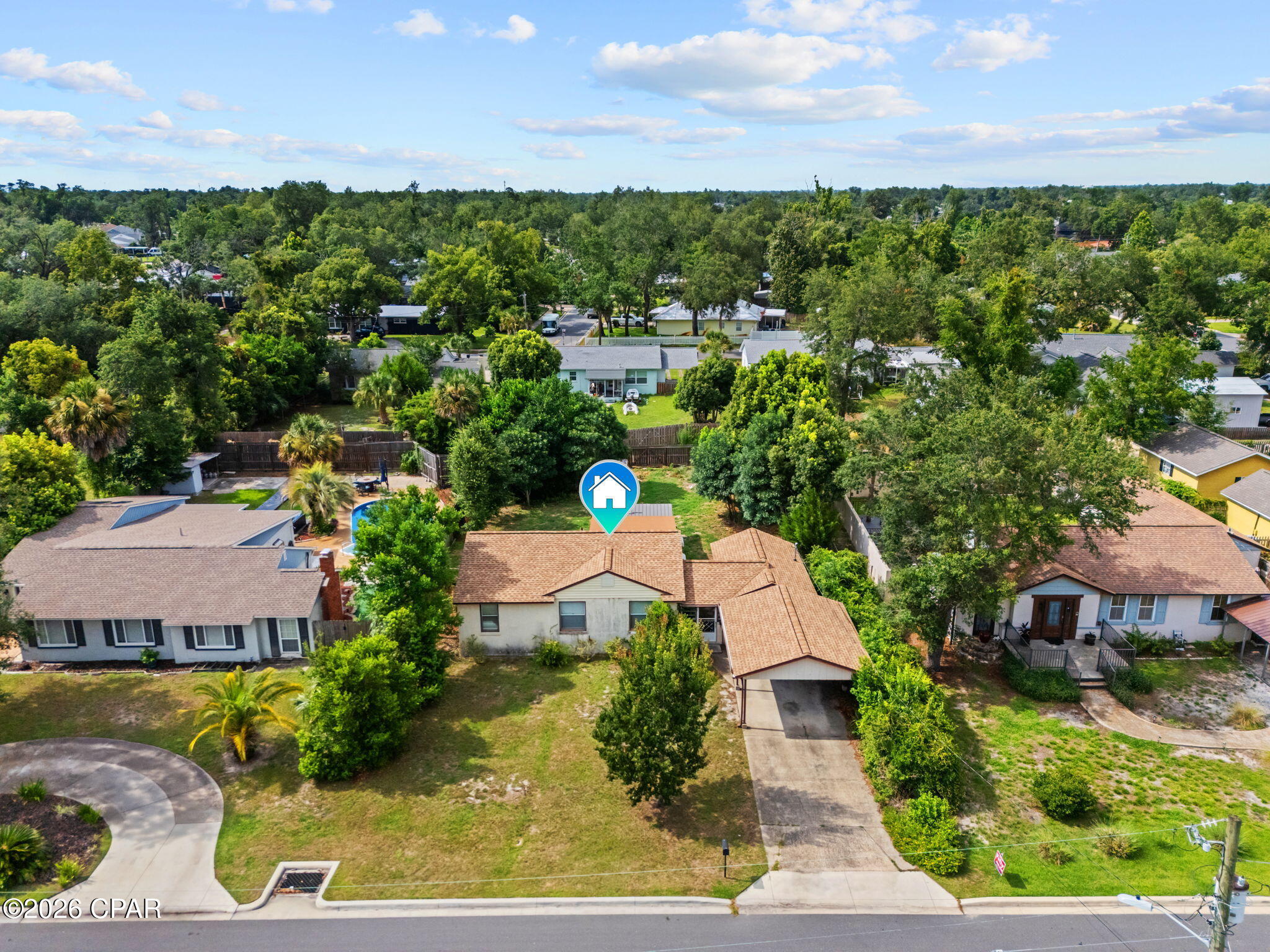 Aerial view of a tan-roofed house marked with a blue home pin, surrounded by tree-lined homes.