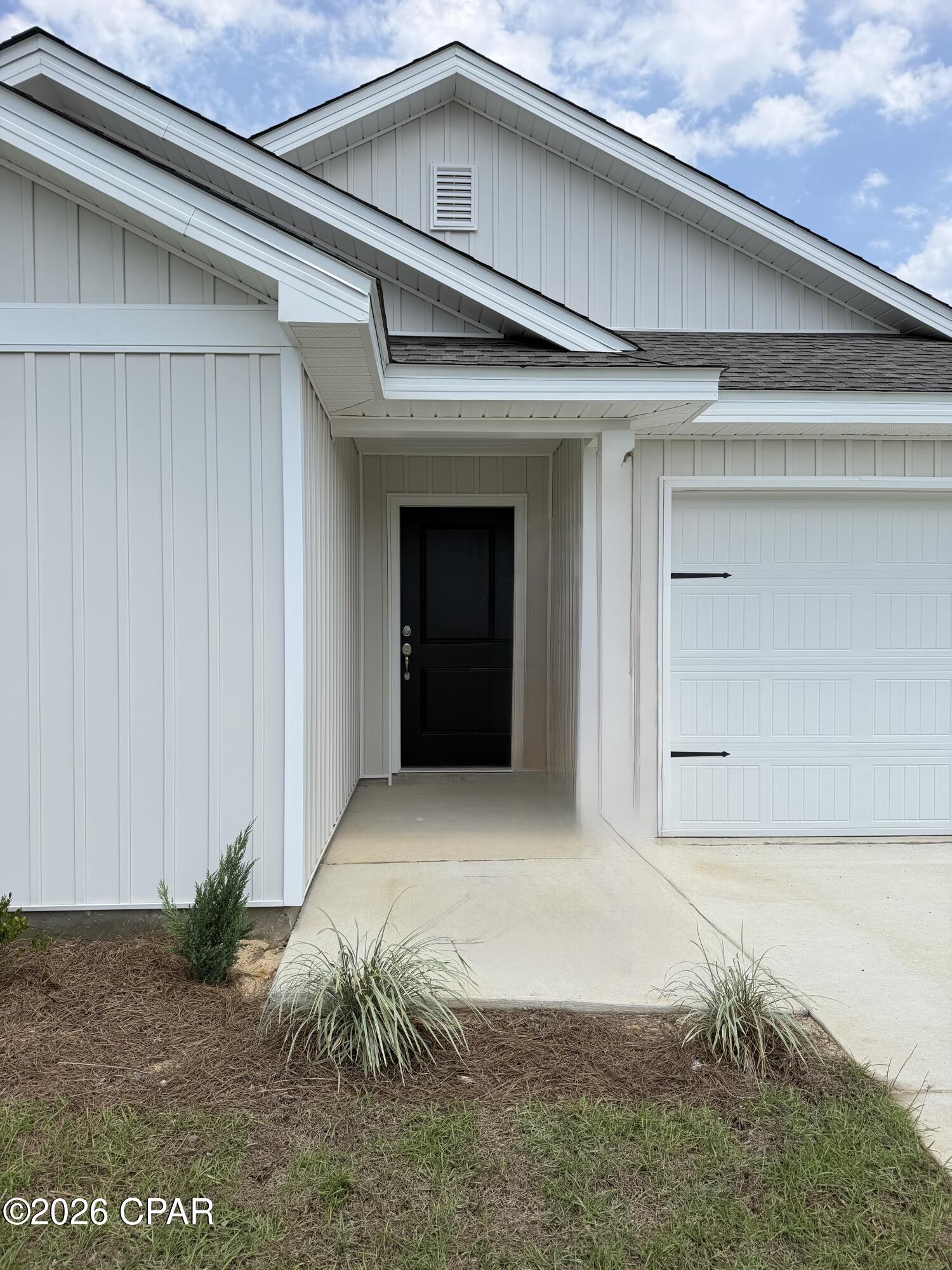 White house entrance with a black front door, covered porch, and attached garage.
