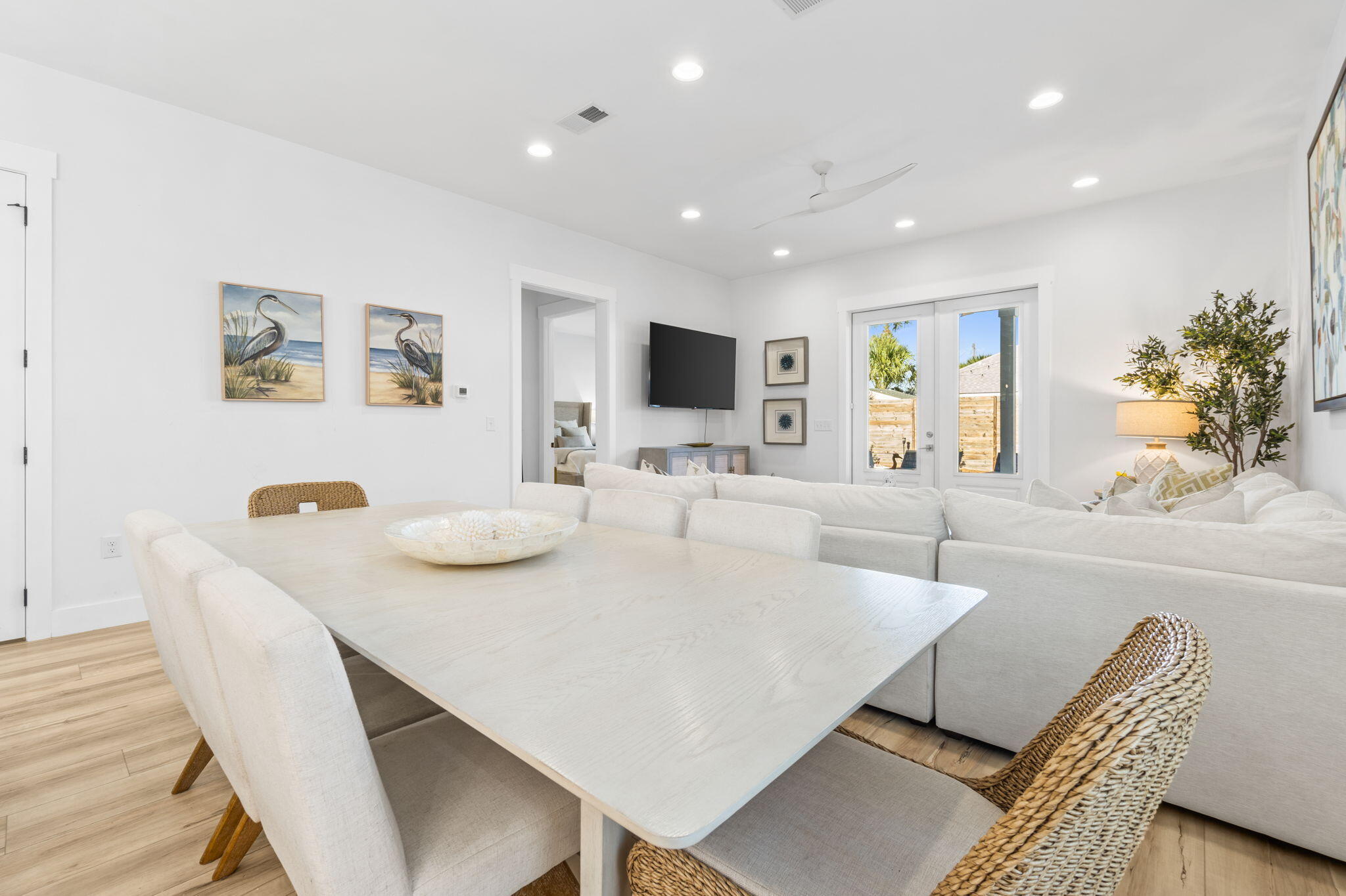 Open-plan living and dining room with a white sectional, large dining table, and glass doors.