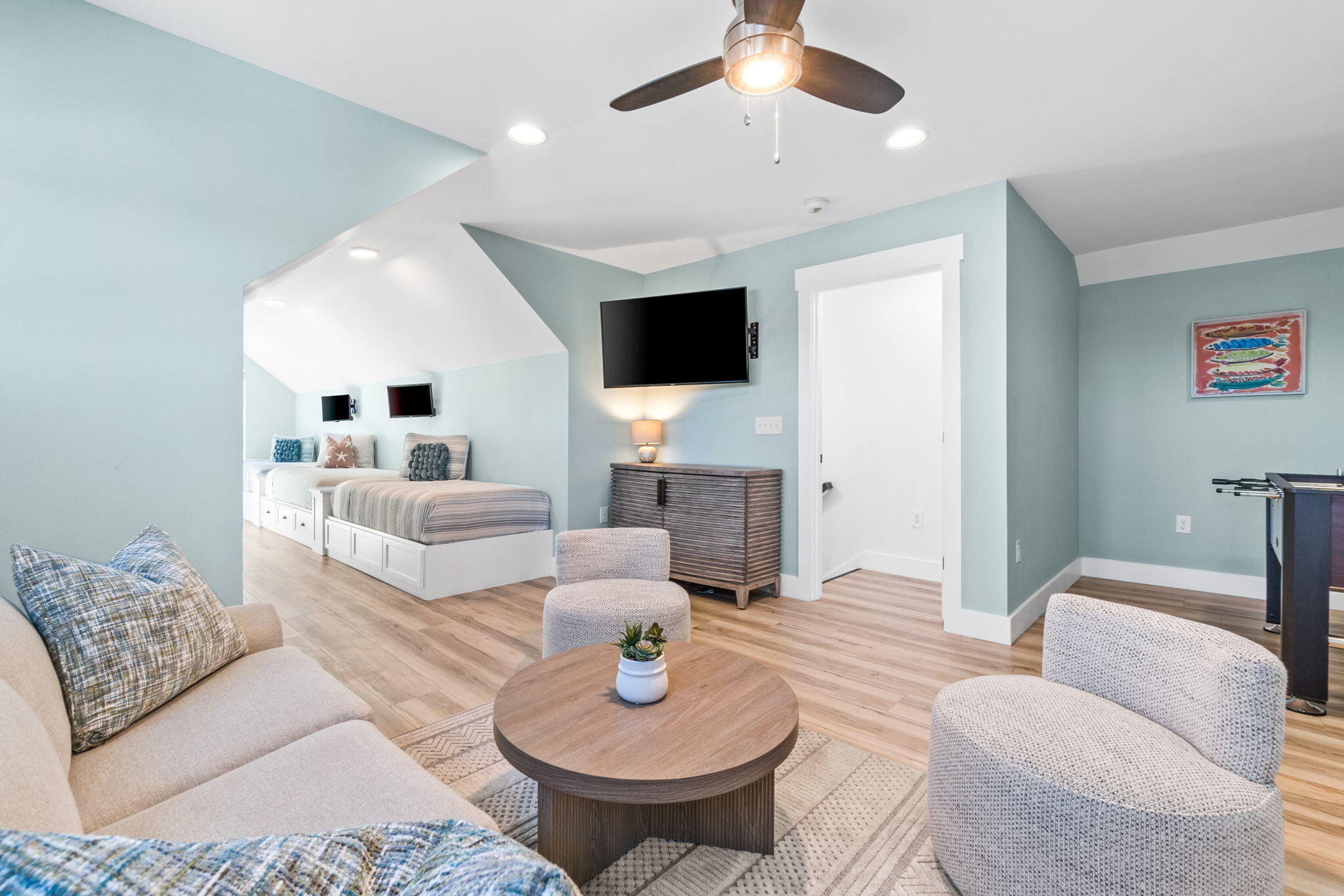 Furnished room with two built-in beds, a sitting area, wall-mounted television, and foosball table.