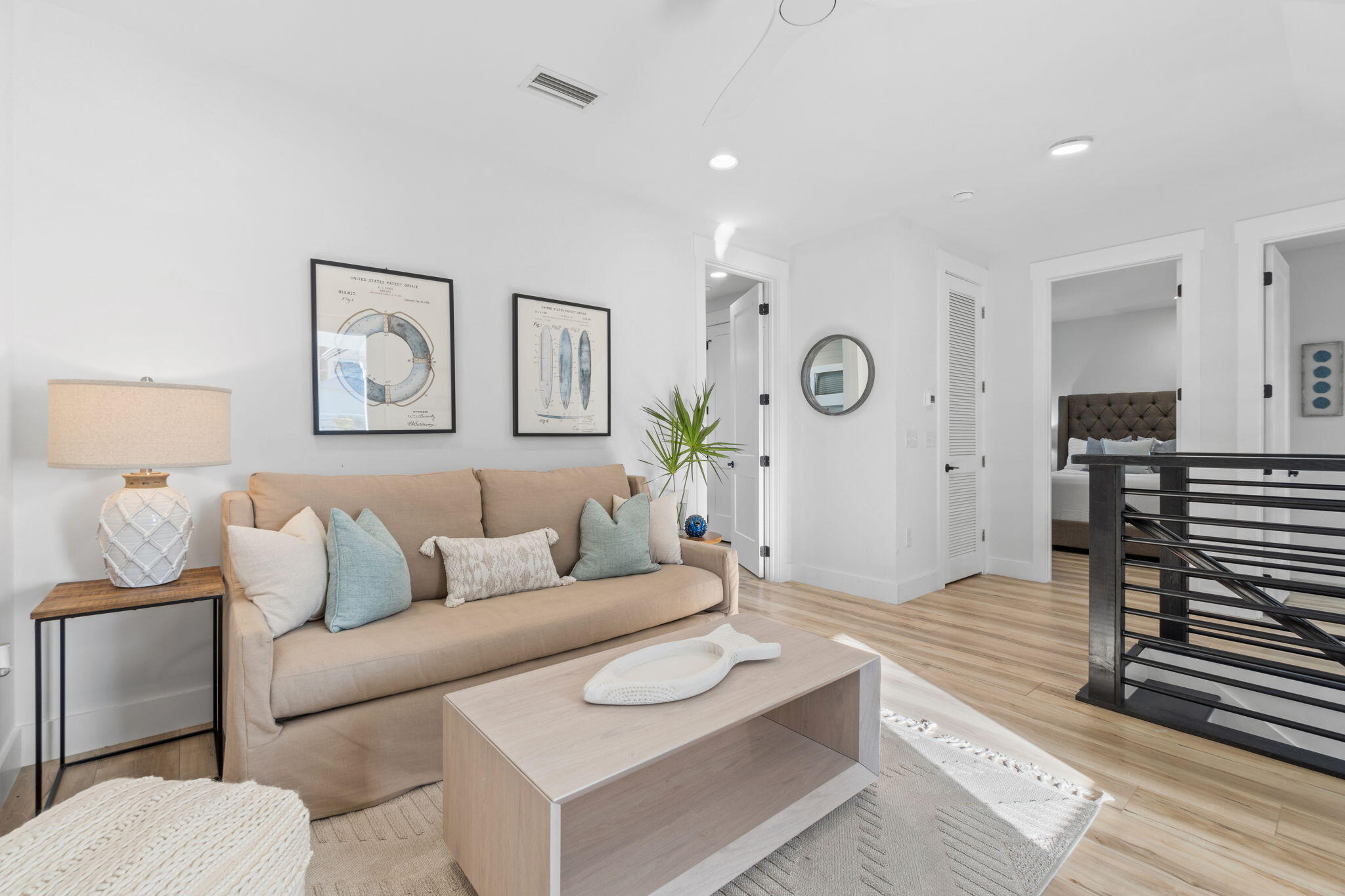 Staged living area with a beige sofa, pale blue pillows, light wood coffee table, and black stair railing.