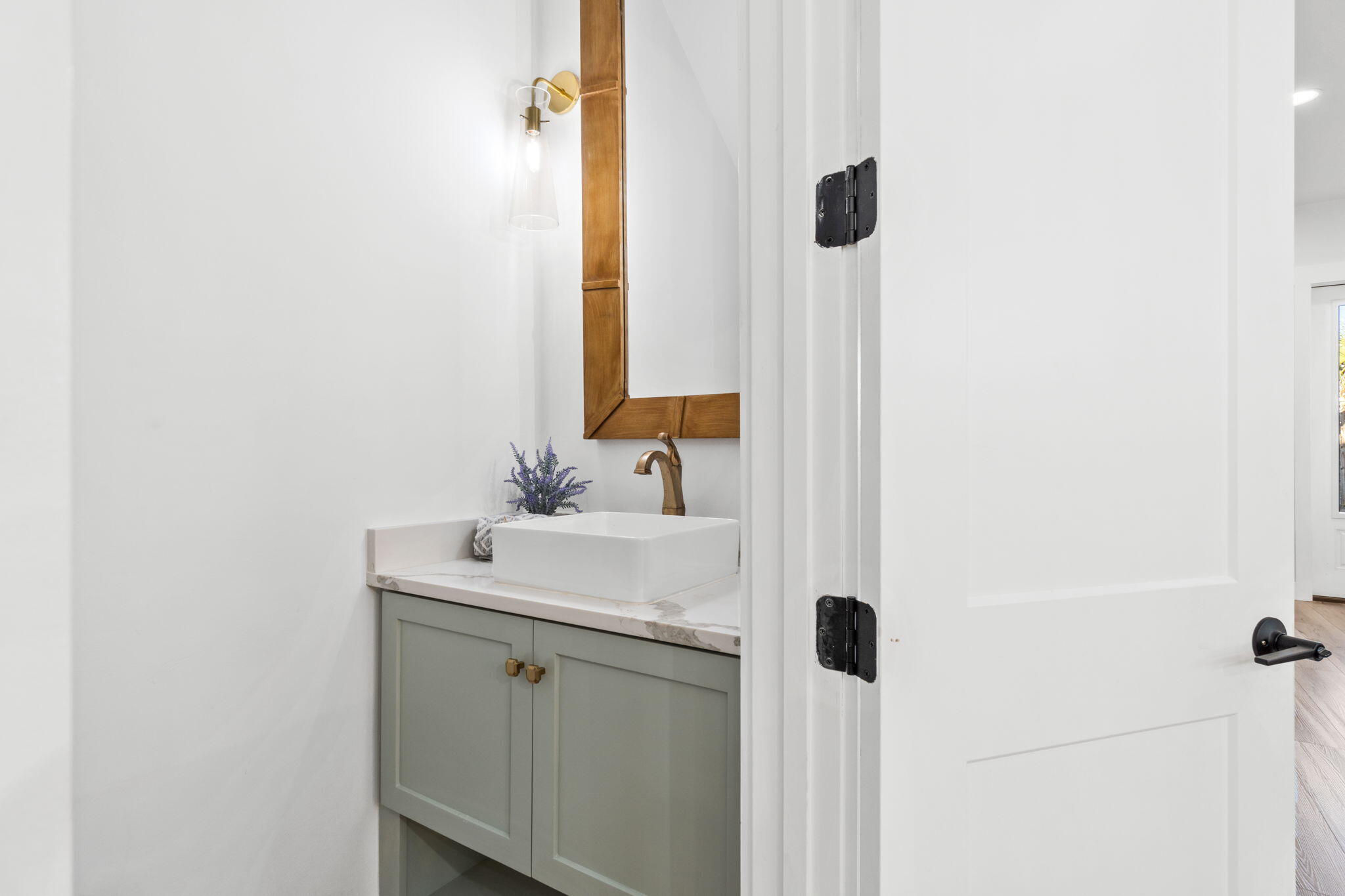Bathroom vanity with a white vessel sink, gray-green cabinet, and wood-framed mirror.