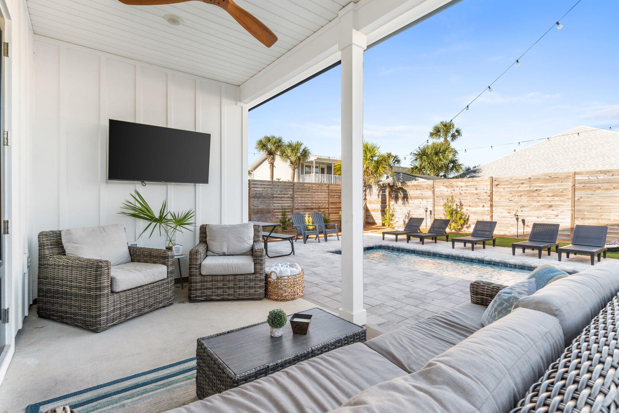 Covered patio with wicker seating and television overlooking a private pool and lounge chairs.