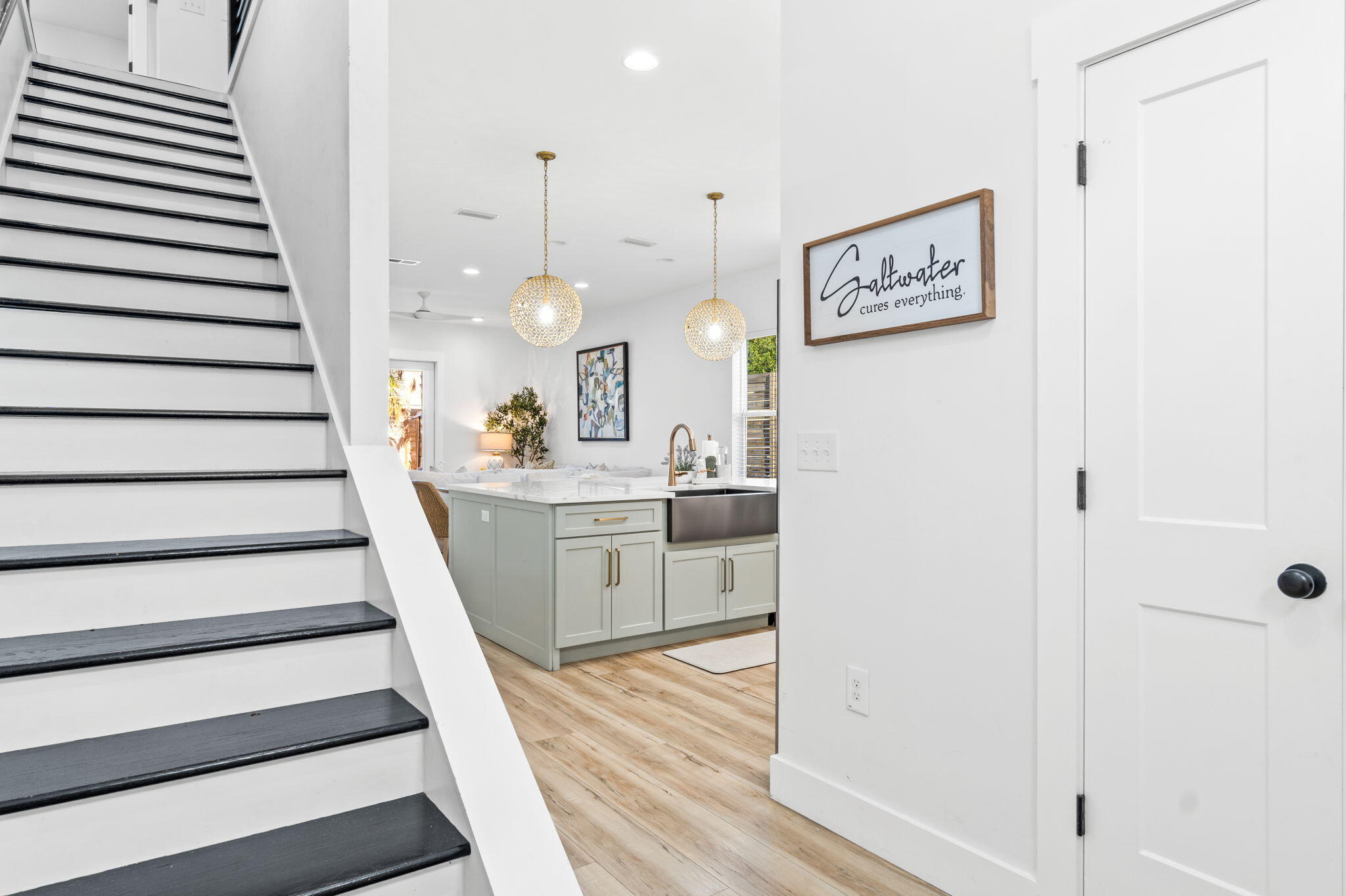 Bright kitchen with sage cabinetry and island beside a black-trimmed staircase.