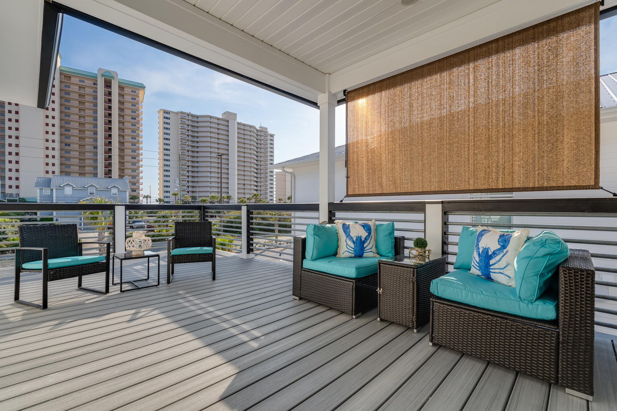 Covered deck with turquoise wicker seating and high-rise buildings beyond the railing.
