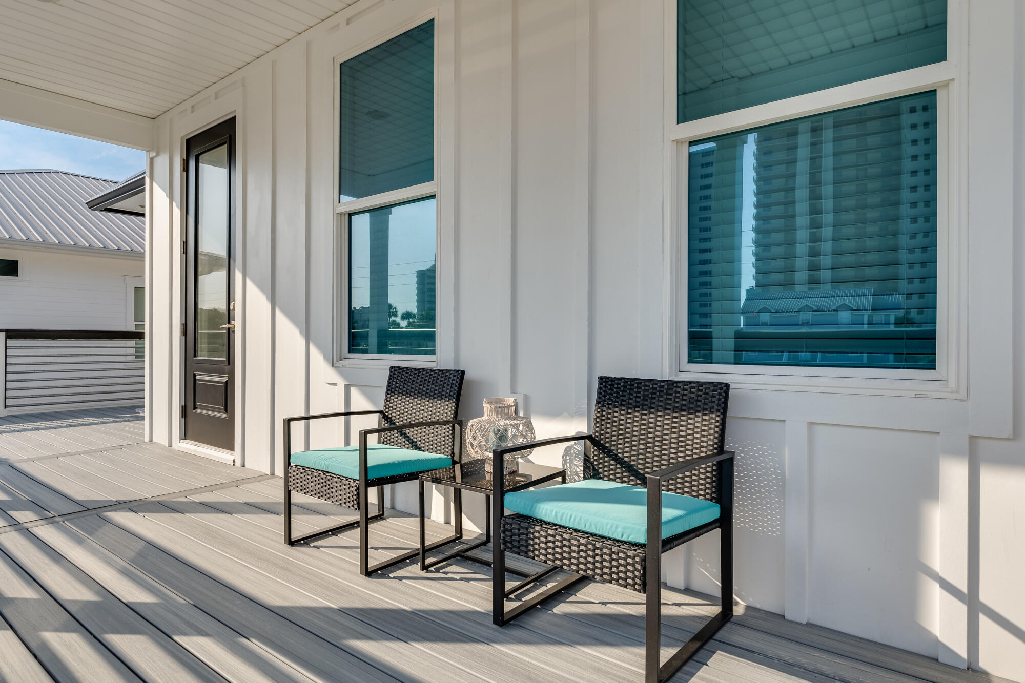 Outdoor deck with two woven chairs and turquoise cushions beside large windows.