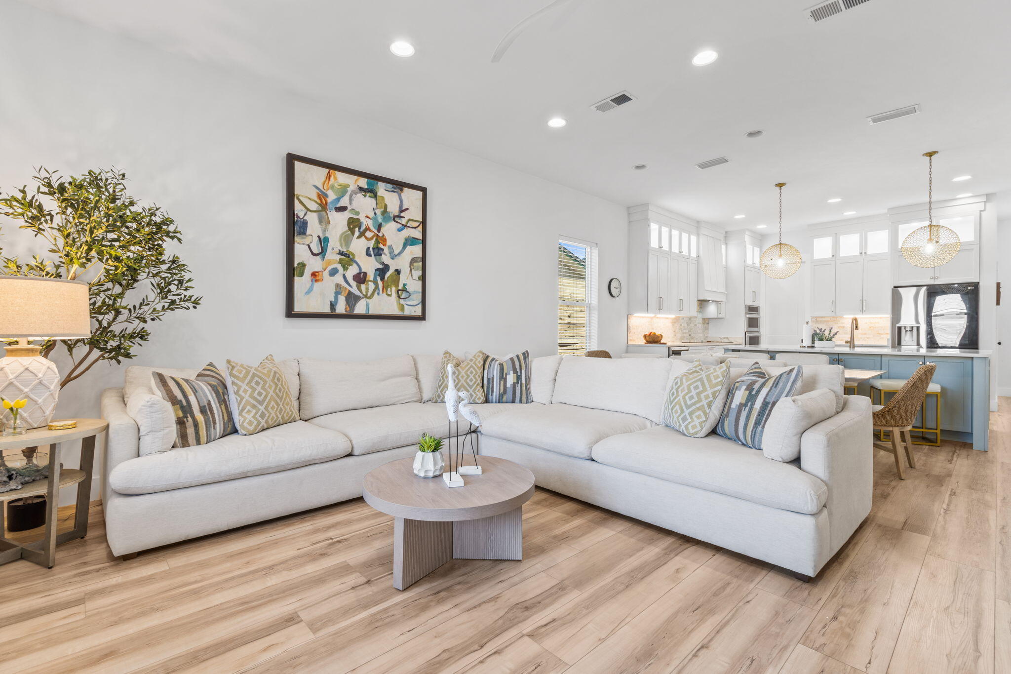 Open-plan living room with a cream sectional sofa and bright kitchen with blue island cabinets.