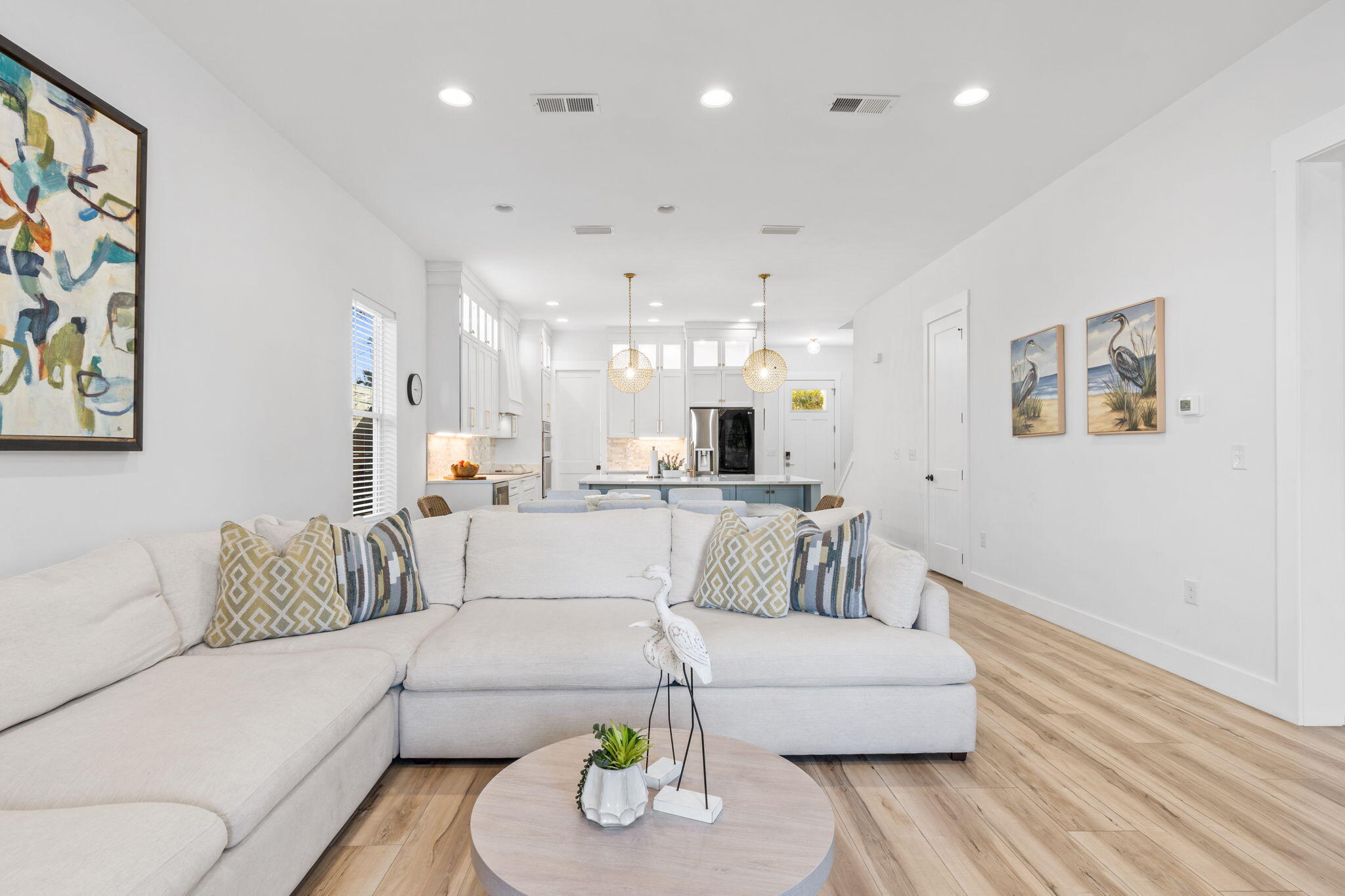 Open-plan living room with a white sectional sofa, wood floors, and kitchen island behind it.