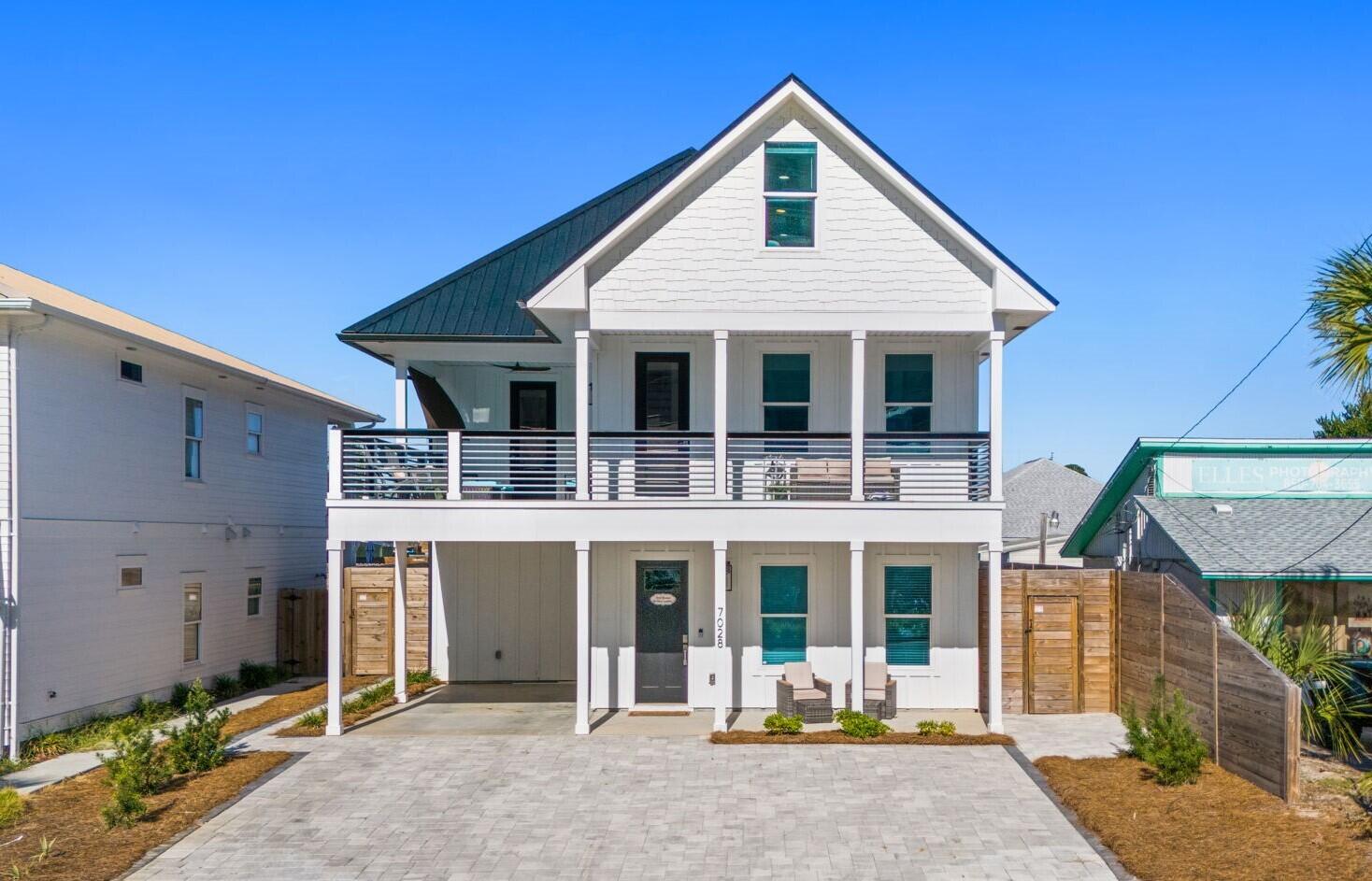 White two-story house with a steep gabled roof, full-width balcony, and paved front drive.