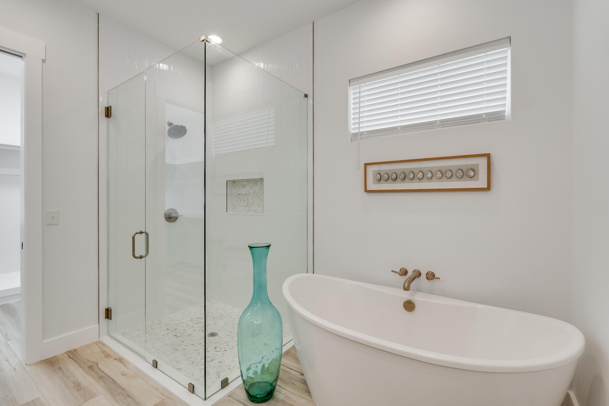 Modern bathroom with a glass walk-in shower, freestanding tub, and turquoise vase.