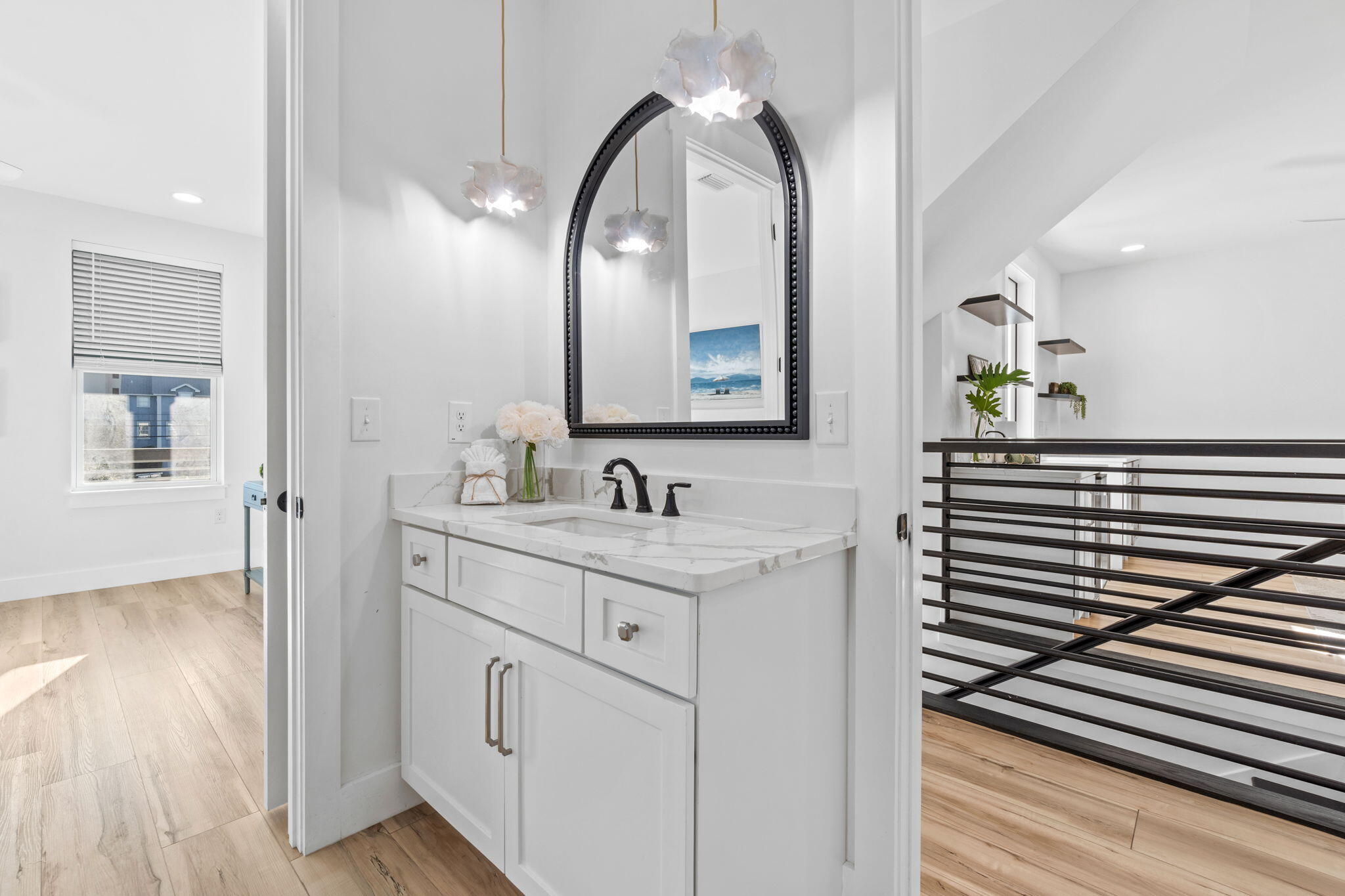 White bathroom vanity with marble countertop and arched mirror beside a black metal stair railing.