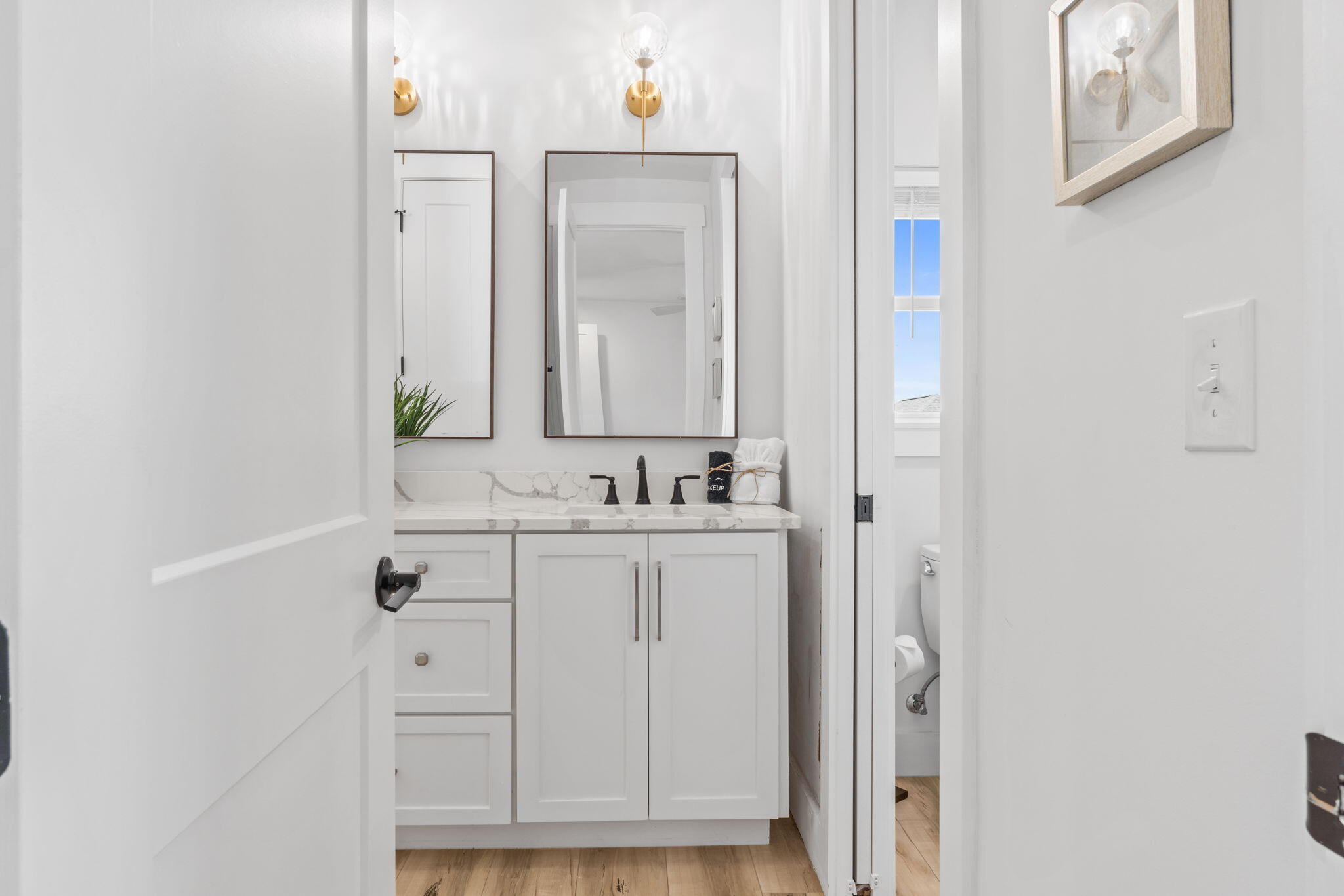 Bathroom vanity with a marble-look counter, black faucet, framed mirrors, and brass wall sconces.