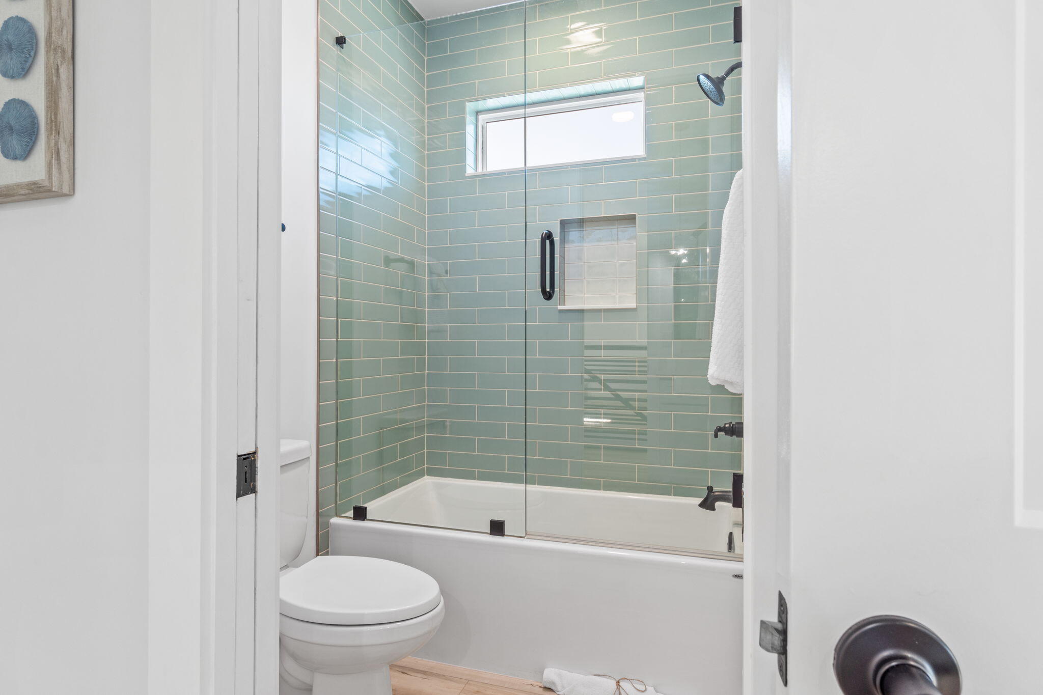 Bathroom with a glass-enclosed tub, sage-green tile, built-in niche, and high window