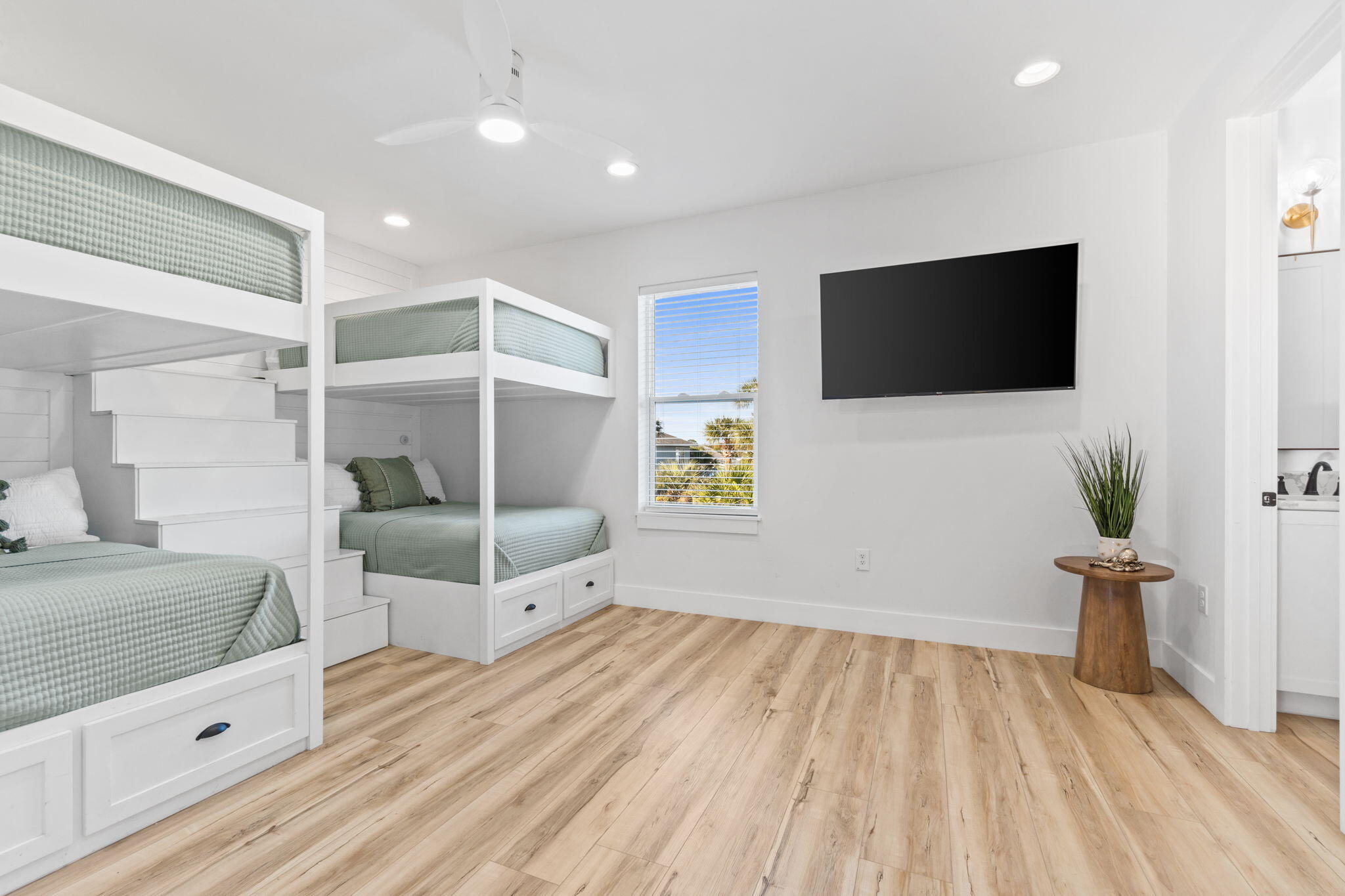 Bright bedroom with white built-in bunk beds, sage bedding, and a wall-mounted TV.