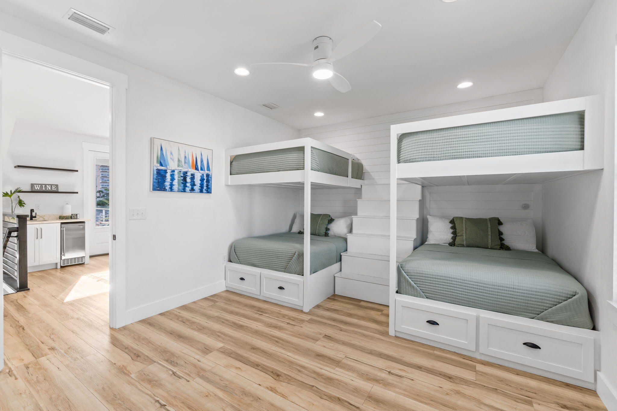 Bedroom with built-in white bunk beds, sage-green bedding, and stairs between the beds.