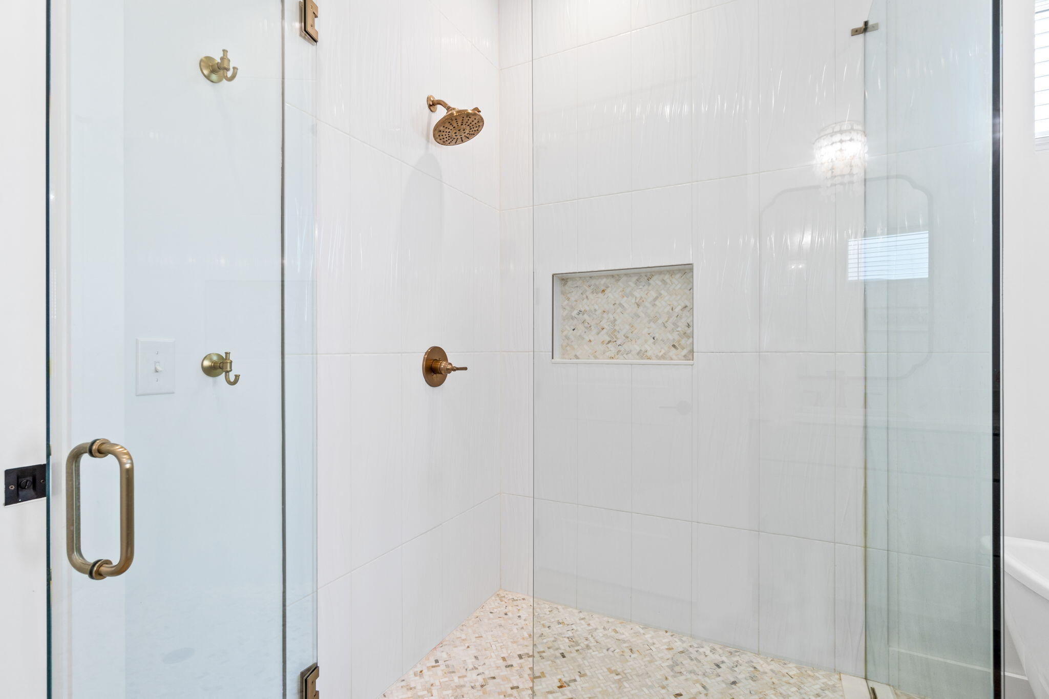 Walk-in shower with clear glass doors, brass fixtures, and a mosaic-tiled niche.
