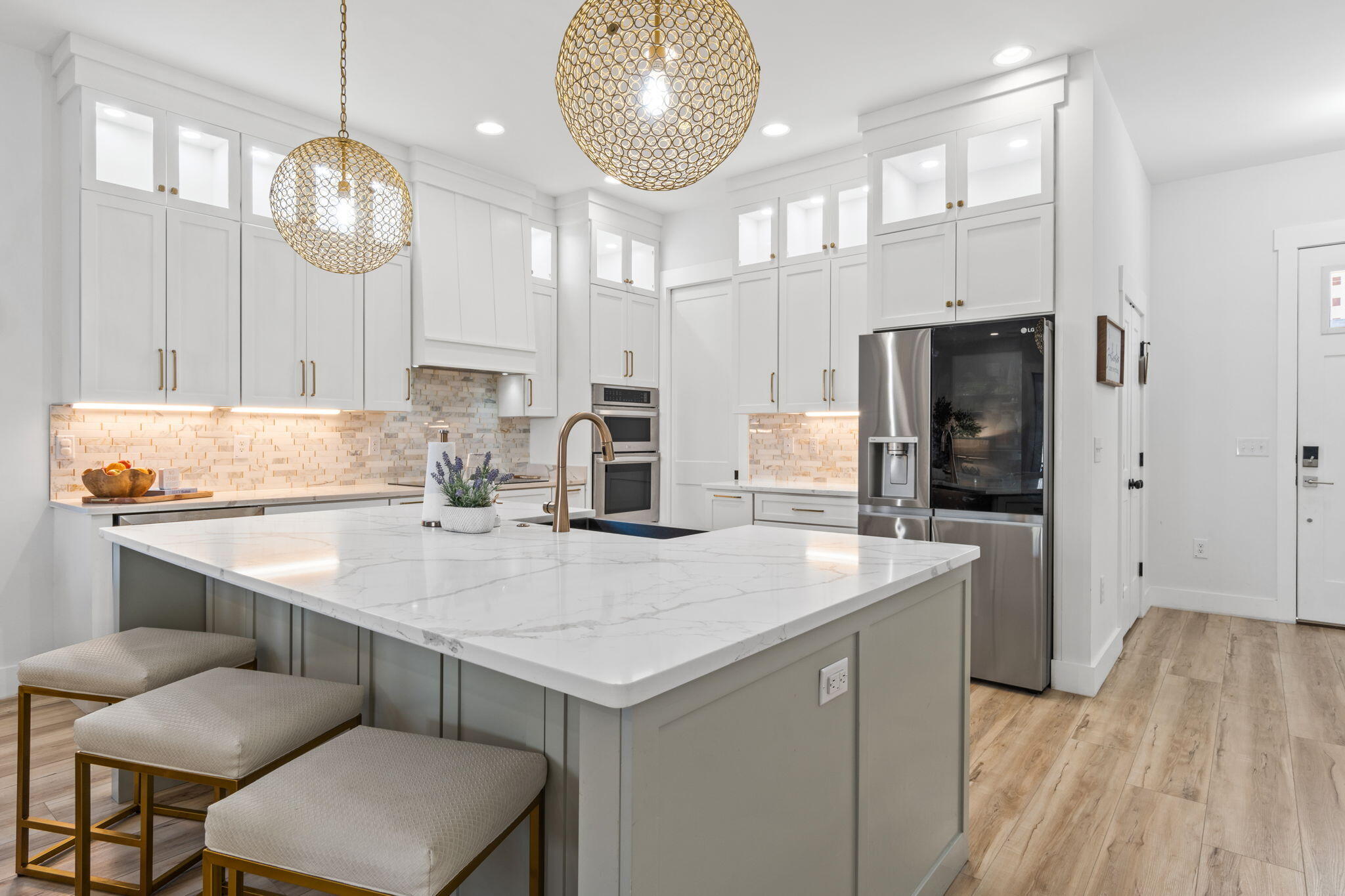 Modern kitchen with a large white island, gold pendant lights, and stainless steel appliances.