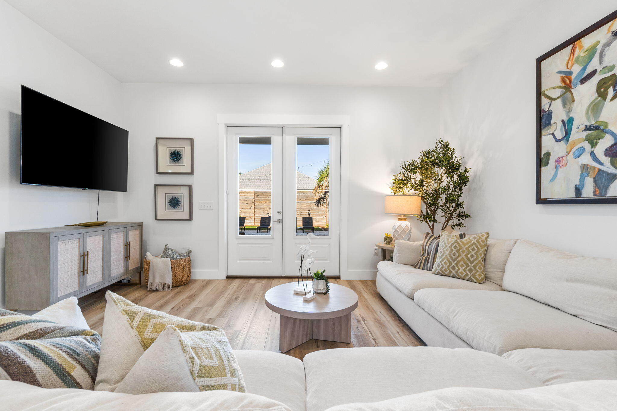 Bright living room with white sectional sofas and French doors opening to a fenced patio.