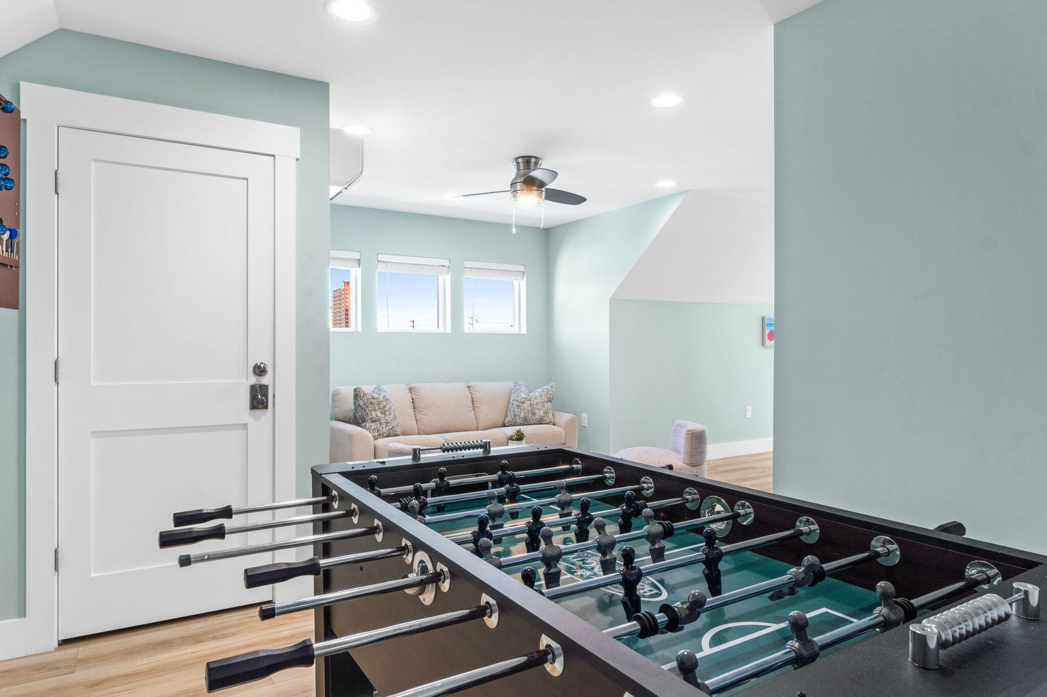 Game room with a foosball table, sofa, and three windows.