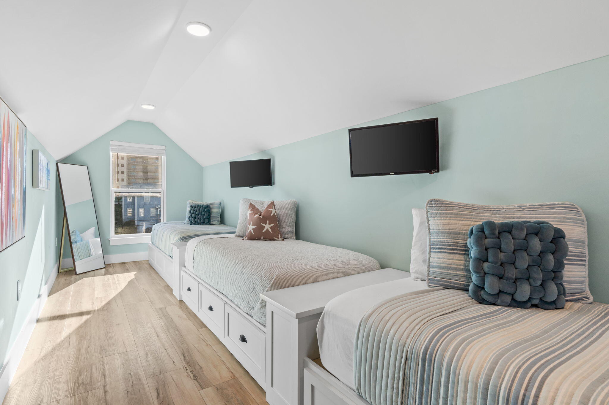 Furnished bedroom with three white twin beds, aqua walls, and two wall-mounted televisions.