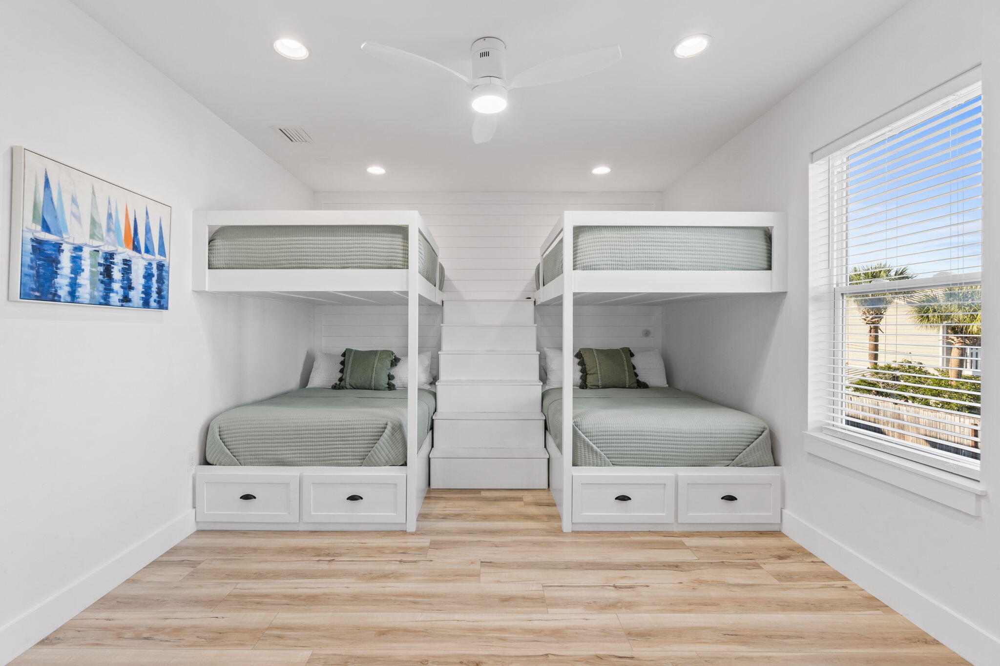 Bedroom with paired built-in bunk beds, central stairs, storage drawers, and a bright window.