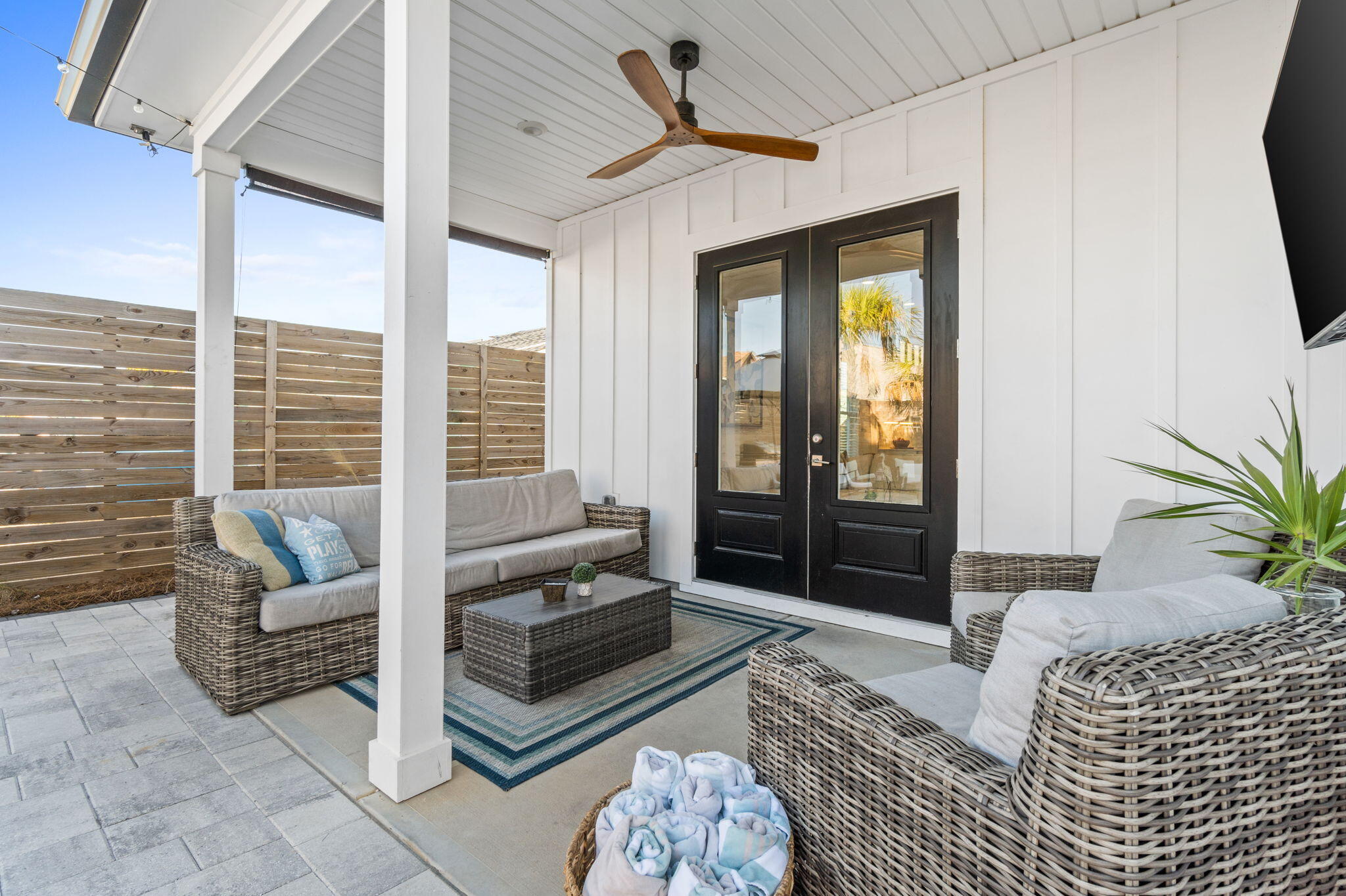 Covered patio with wicker seating, a striped rug, and black double doors.